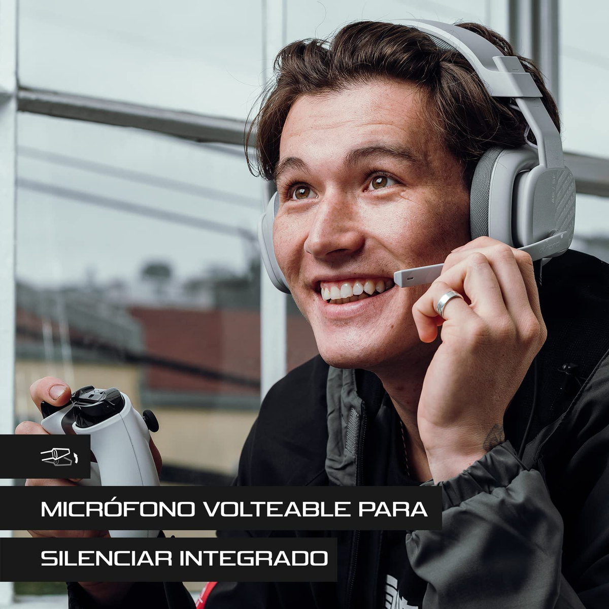 Młody mężczyzna w zestawie słuchawkowym z mikrofonem, trzymający kontroler, uśmiechnięty.