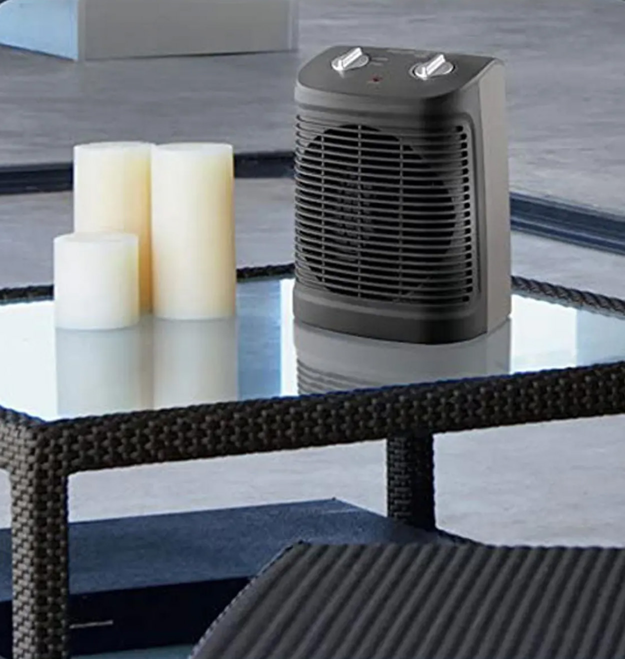 Czarny grzejnik elektryczny na szklanym stoliku ze świecami. Czarna ramka i jasne tło.