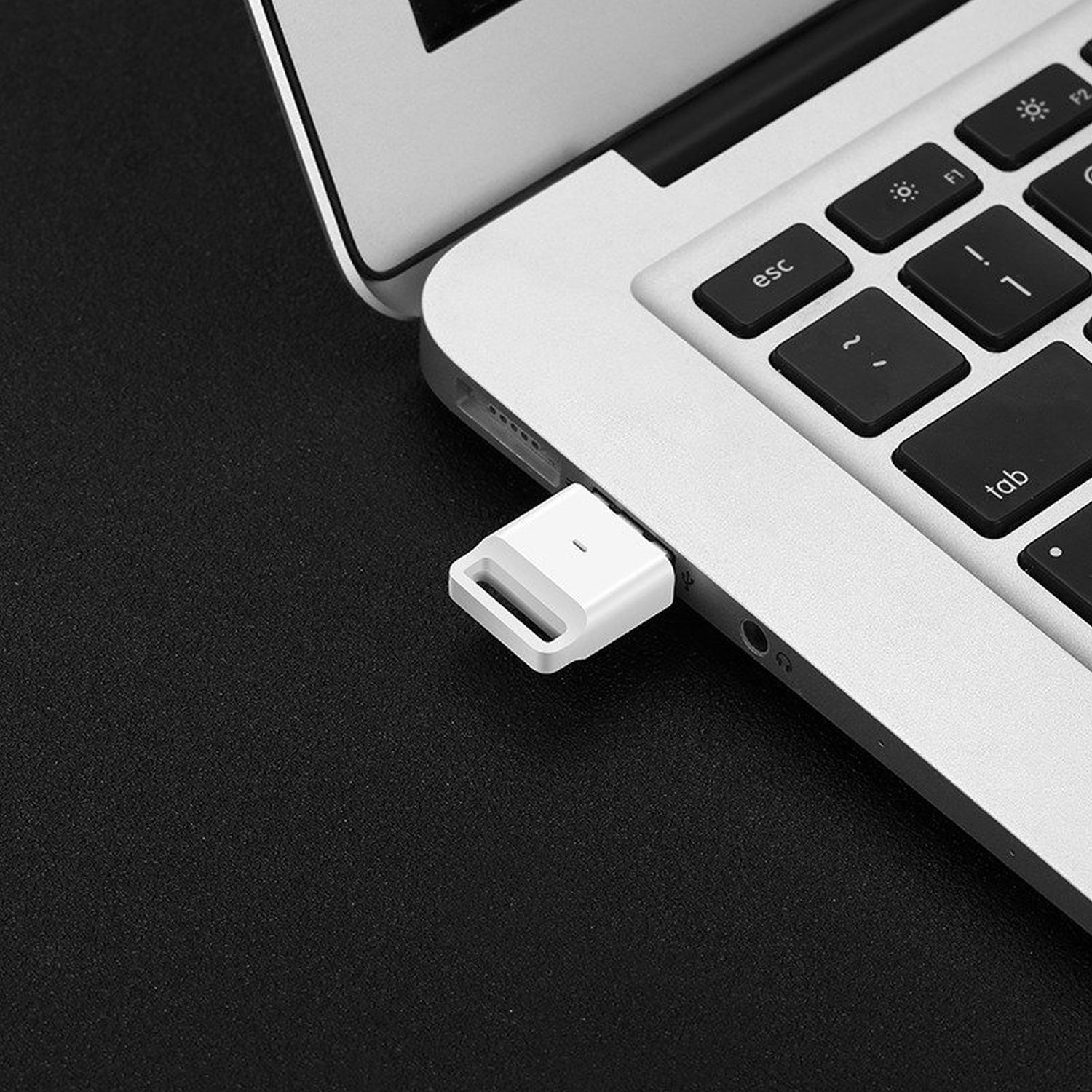Weißer USB-C-Adapter, der in einen silbernen Laptop eingesteckt ist. Schwarzer Hintergrund.