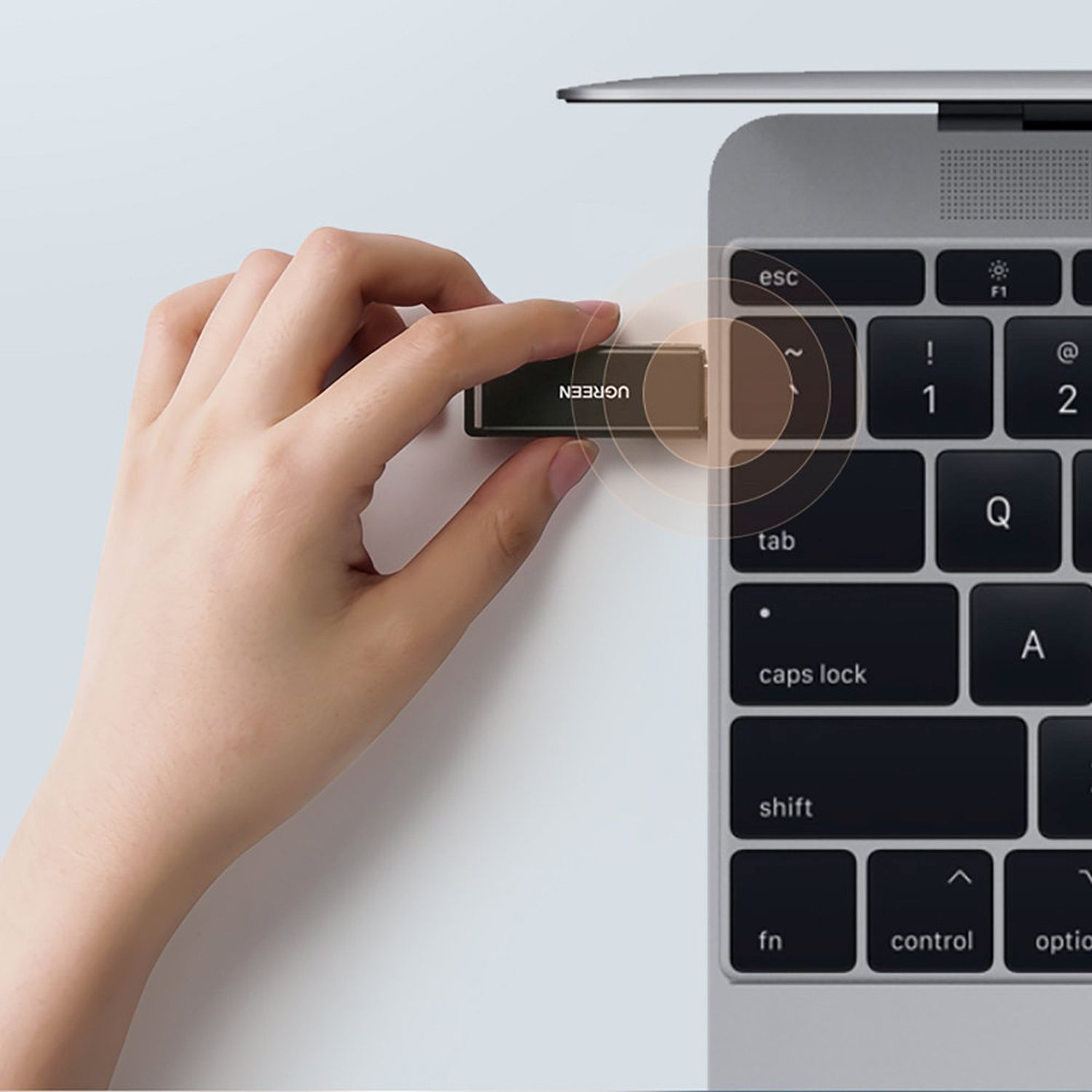 Ręka umieszczająca adapter USB-C UGREEN na klawiaturze laptopa, zbliżenie.