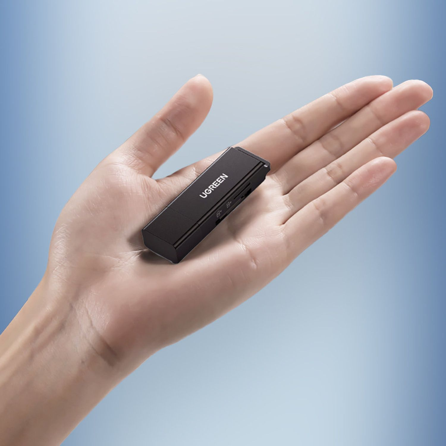 Czarny pendrive UGREEN trzymany w dłoni, na niebieskim tle.