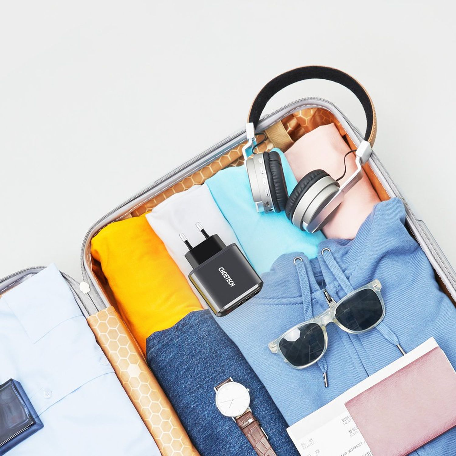 Offener Koffer mit Kleidung, Ladegerät, Kopfhörern, Sonnenbrille und einer Uhr.