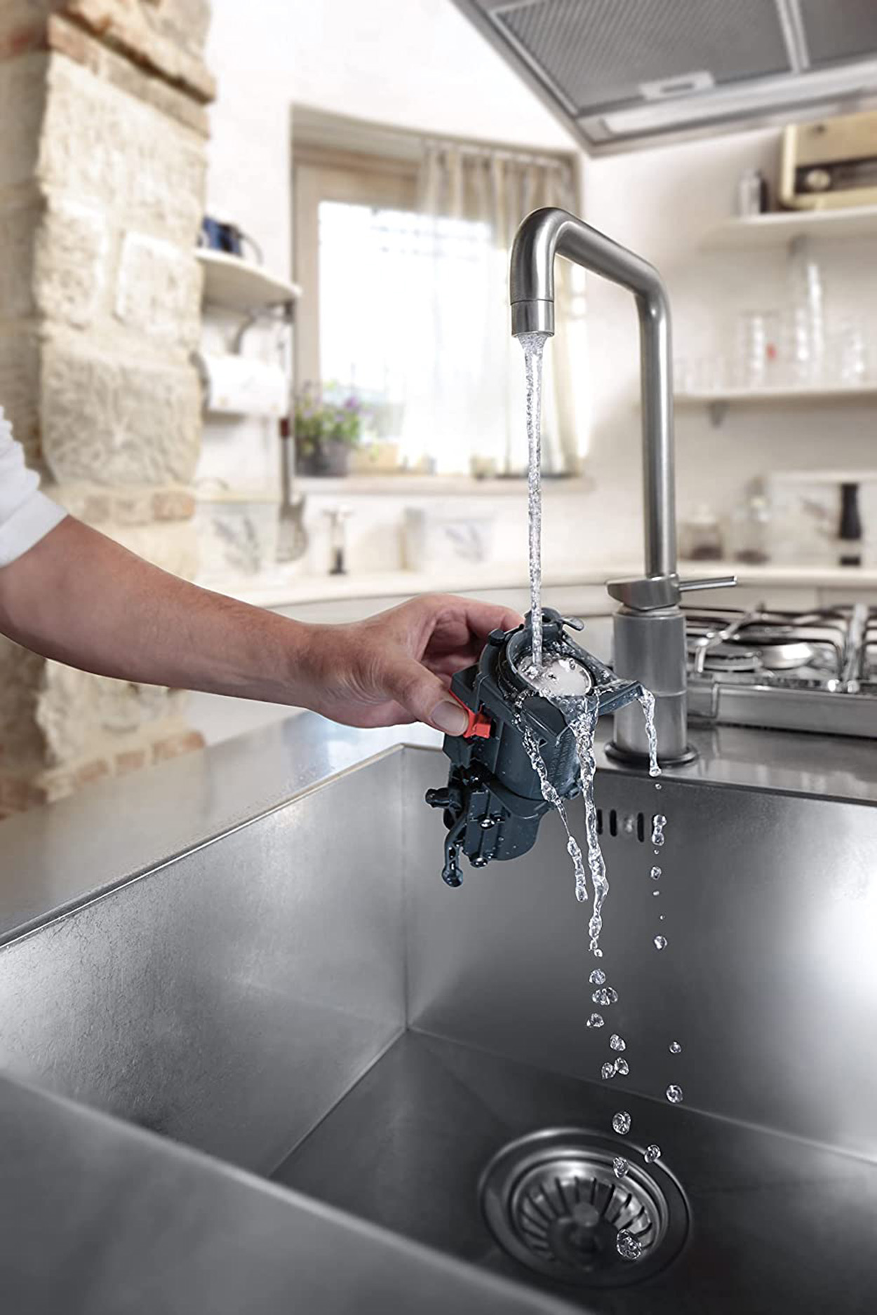 Ręka osoby trzyma część pod bieżącą wodą z chromowanej baterii nad zlewozmywakiem ze stali nierdzewnej.
