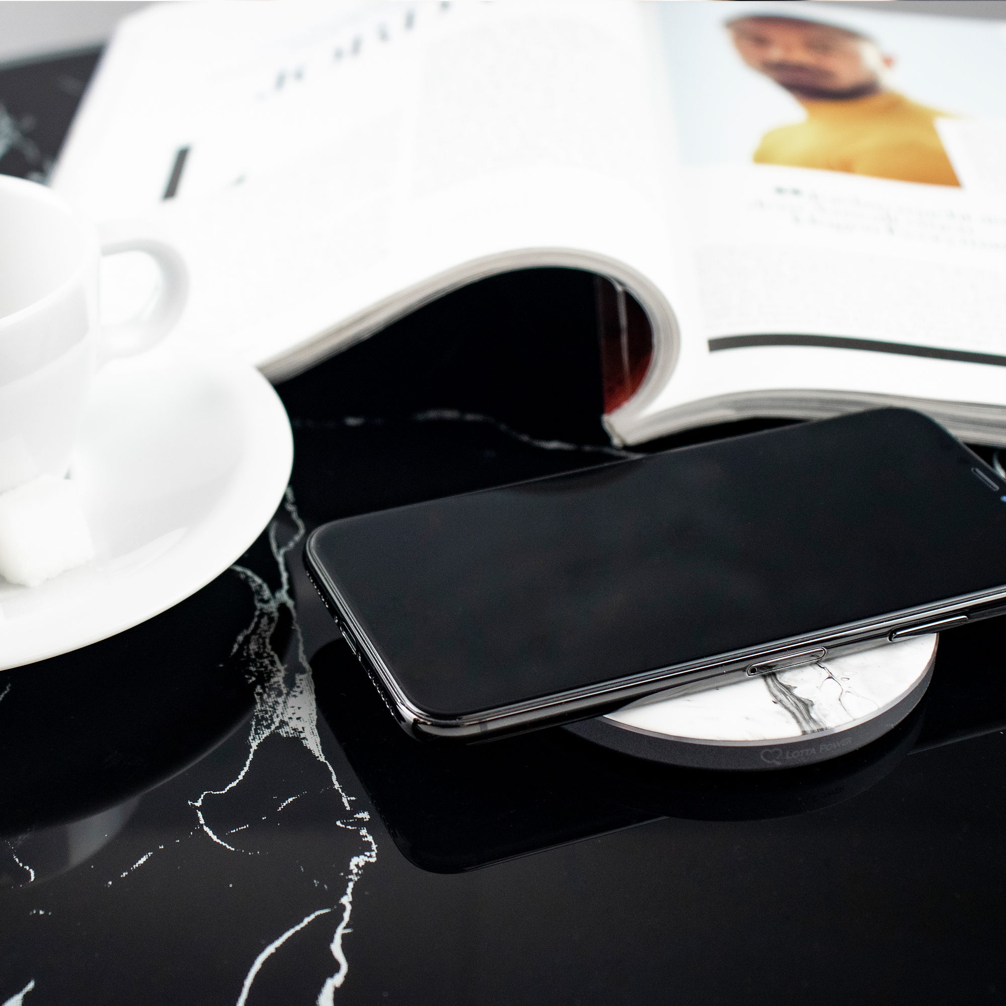 Schwarzes Telefon auf kabellosem Ladegerät auf schwarz-weißem Marmor.