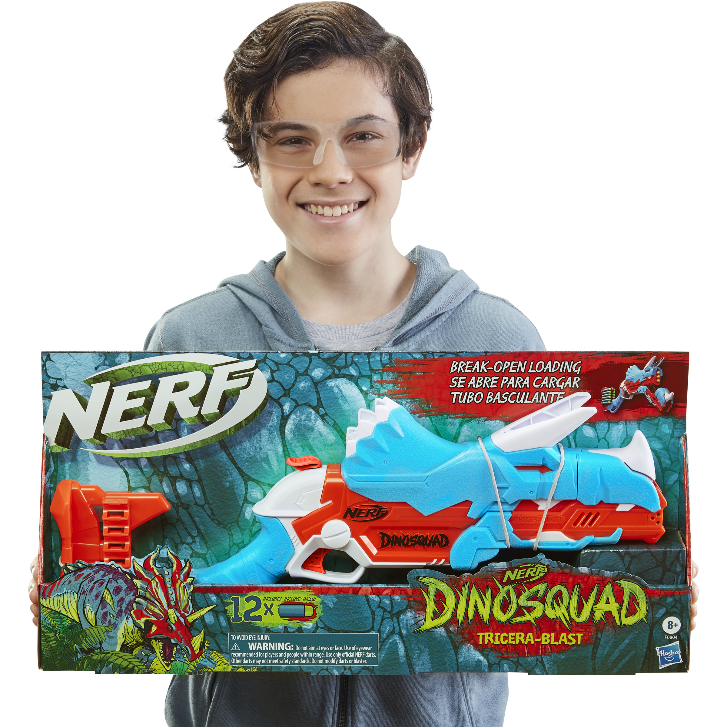 Un niño sostiene una caja de juguetes Nerf Dinosquad Tricera-Blast, sonriendo. La caja es azul, naranja y blanca.
