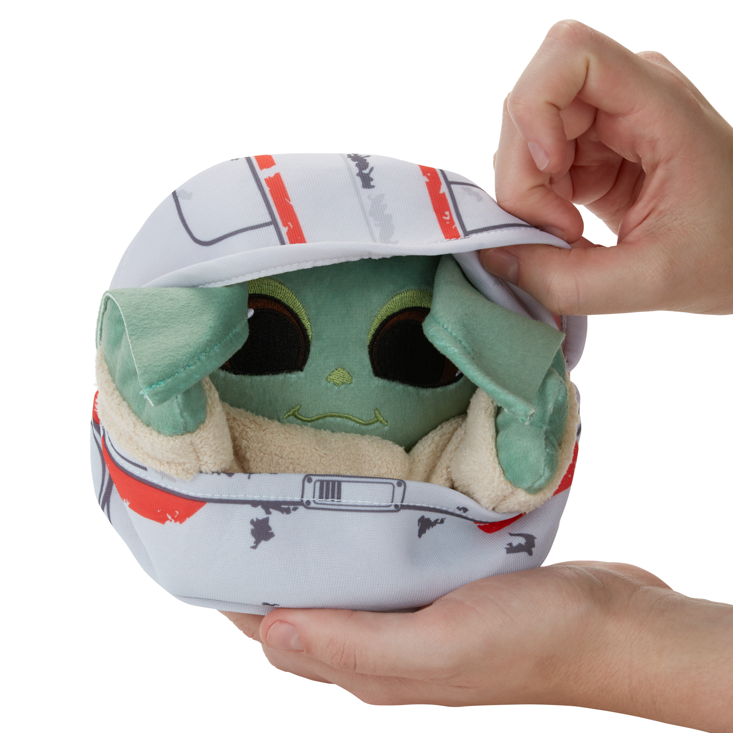 Peluche de Grogu (Baby Yoda) en un capullo, sostenido por dos manos.