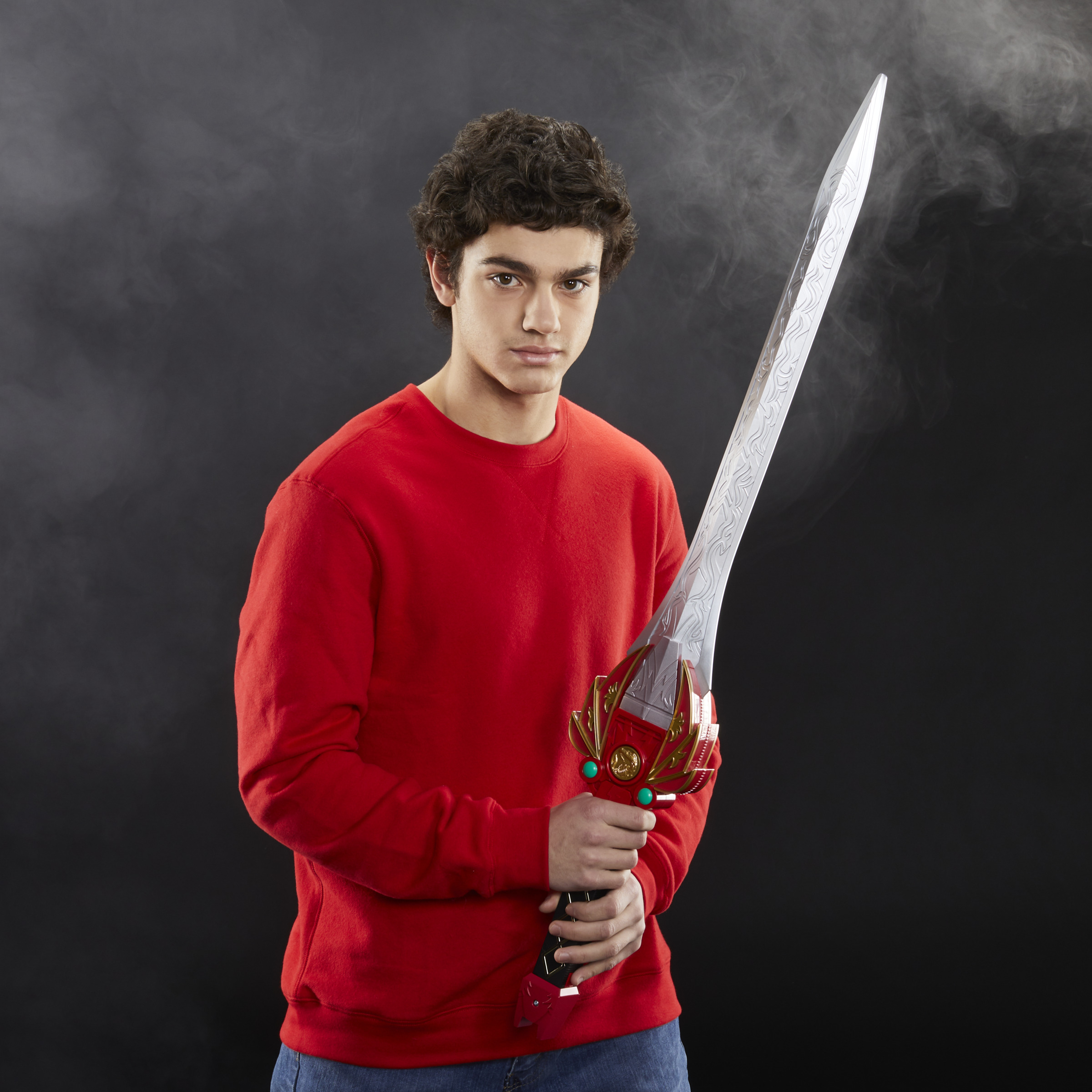 Un joven sostiene una espada plateada con empuñadura roja. Viste un suéter rojo. Fondo negro.