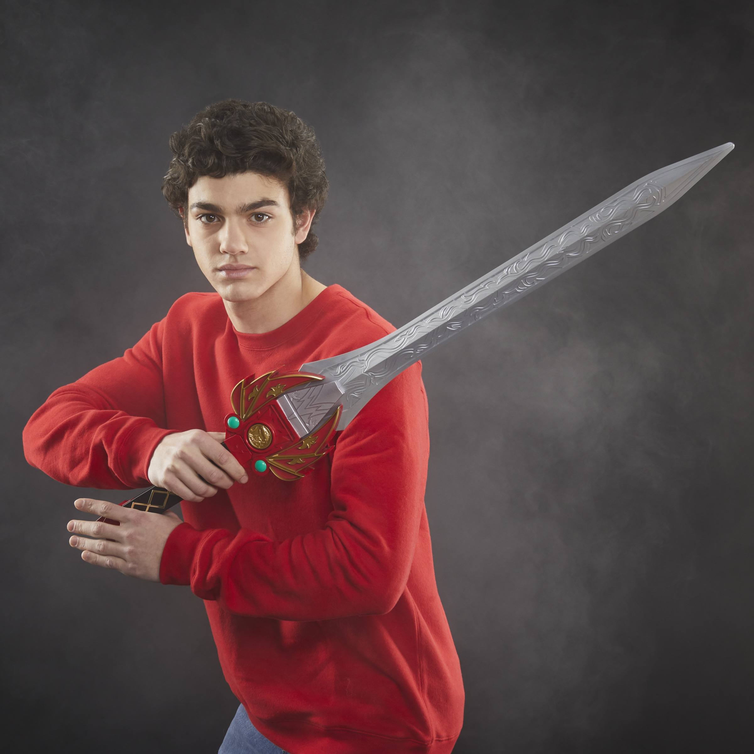 Un joven con un suéter rojo sostiene una espada plateada con un mango verde y dorado.