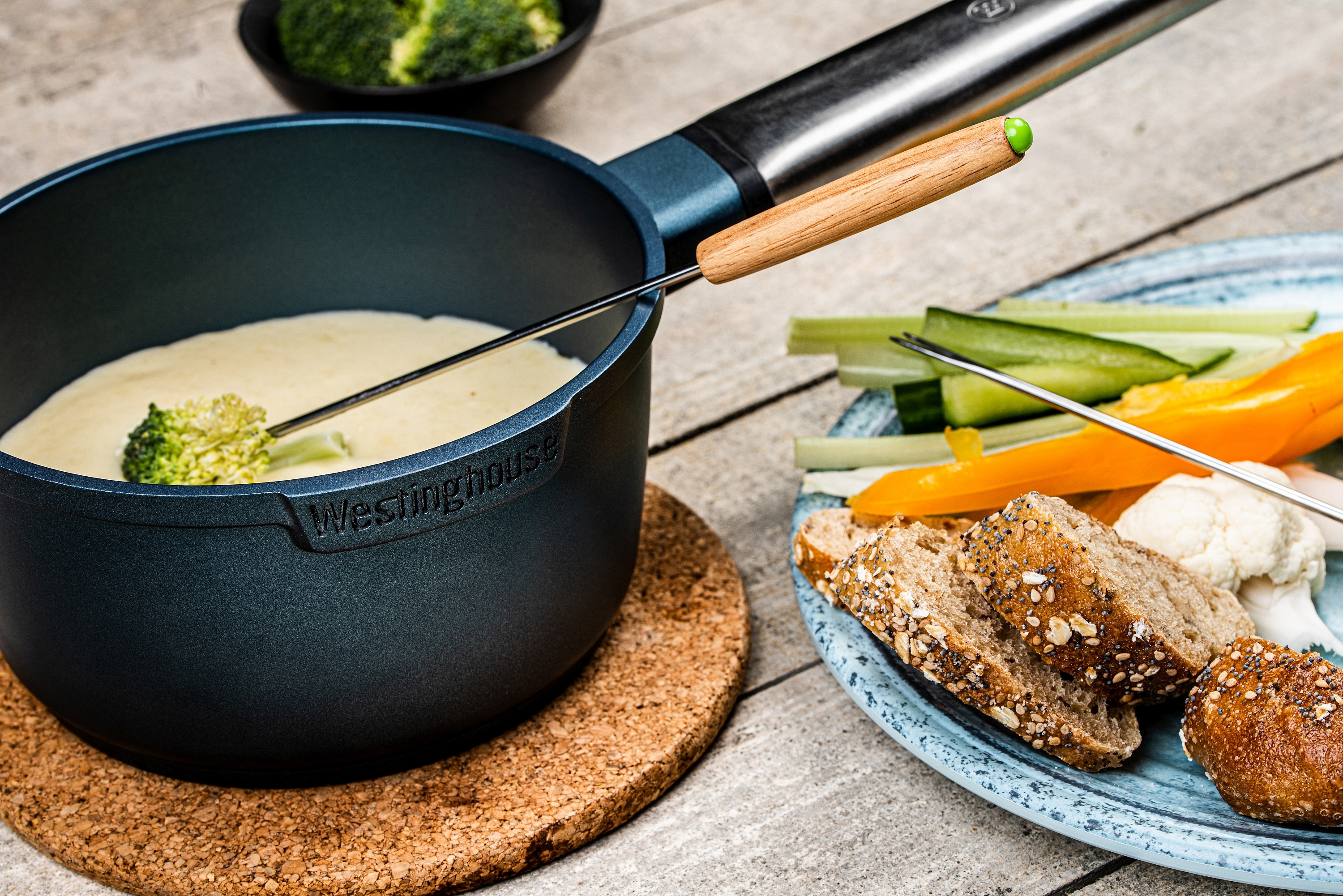 Ein Fonduetopf mit Käse und einer Brokkoliröschen. Brotscheiben, Karotten und Blumenkohl sind auf einem Teller.