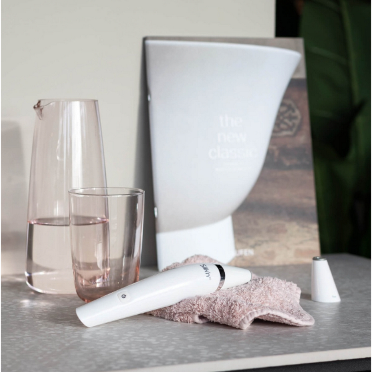 Stilleben: ein Krug und ein Glas mit rosa Flüssigkeit, ein weißes Gerät auf einem Handtuch und ein Buch.