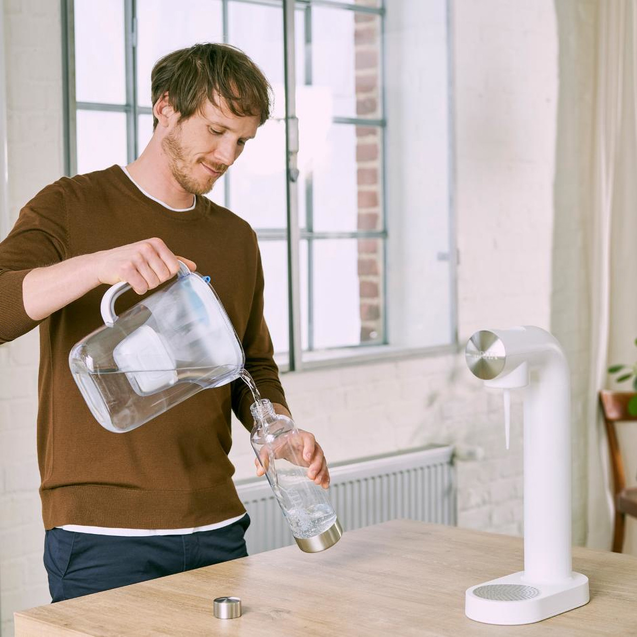 Mann gießt Wasser aus einem Krug in eine Glasflasche. Weißer Spender im Hintergrund.