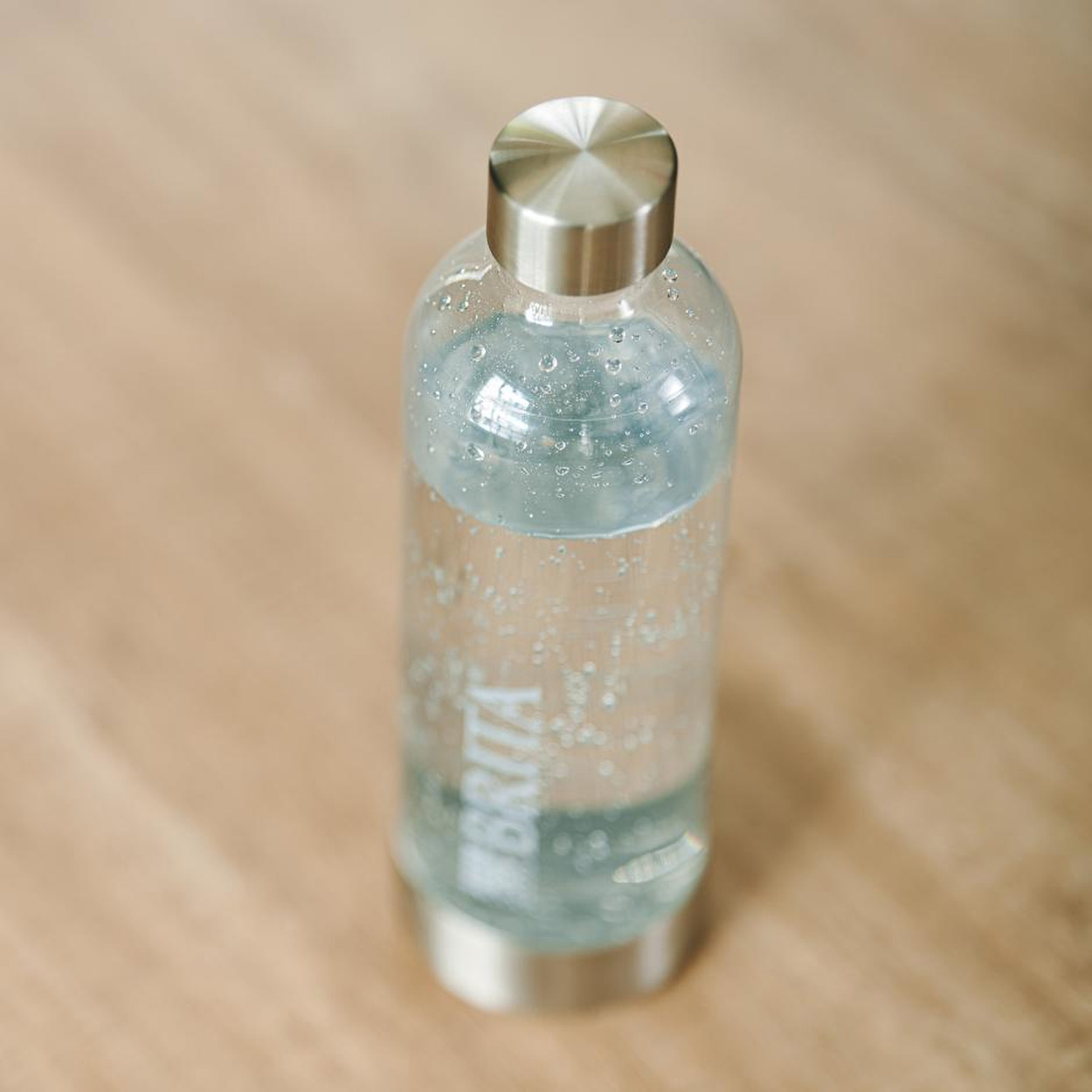 Eine klare Wasserflasche mit silbernem Deckel. Die Flasche ist mit Wasser gefüllt und steht auf Holz.