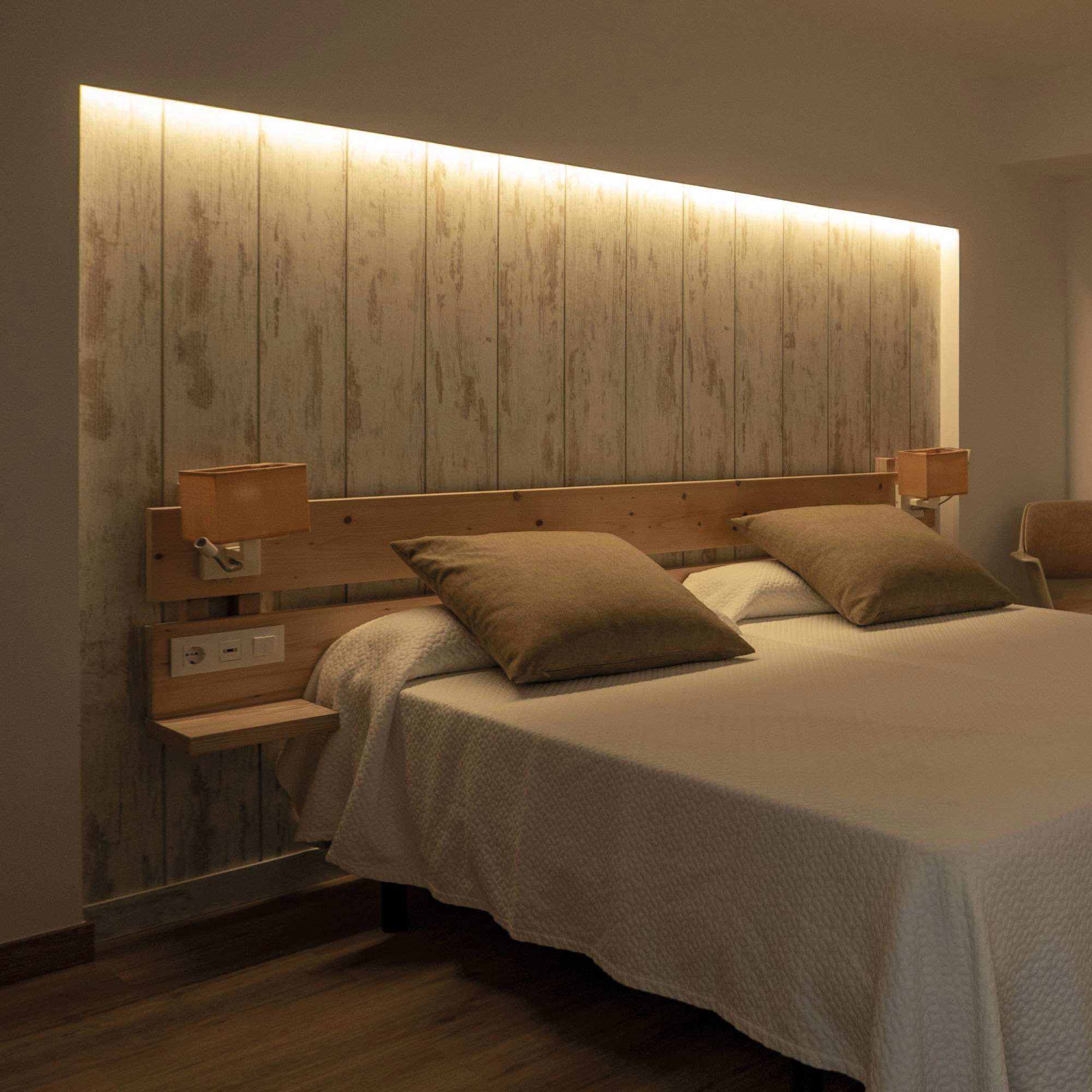Dormitorio con cama. Cabecero de madera con luces y almohadas en la cama.