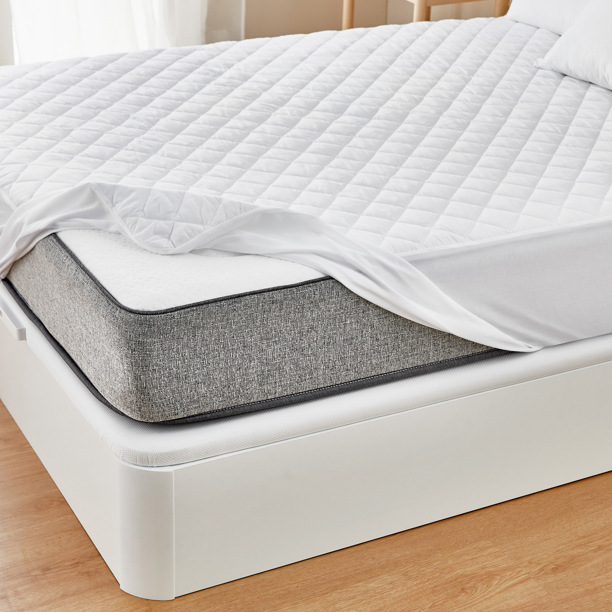 Cama con protector de colchón blanco sobre un colchón gris.