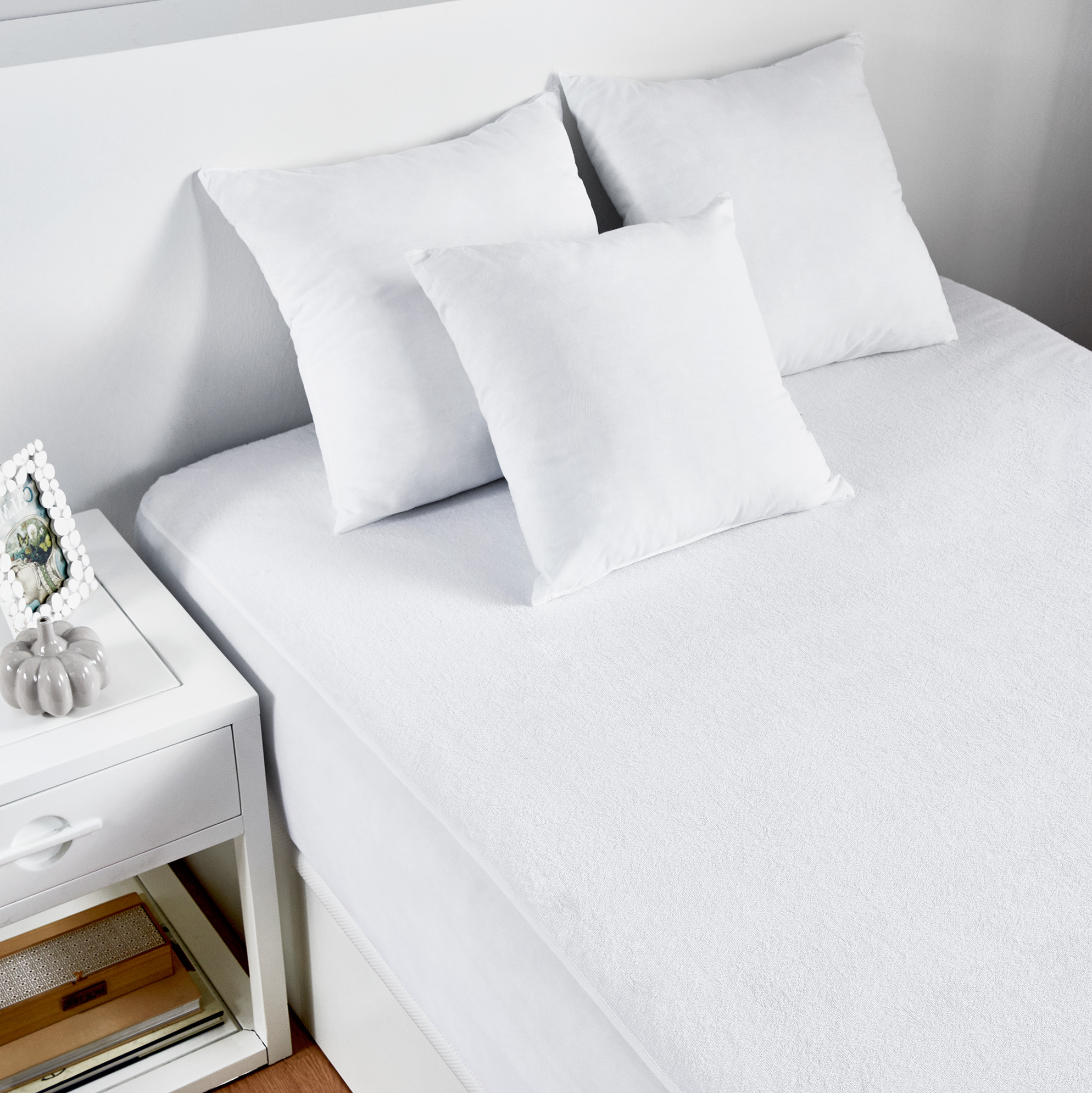 Cama con ropa de cama blanca, incluyendo almohadas. Mesita de noche con decoración.