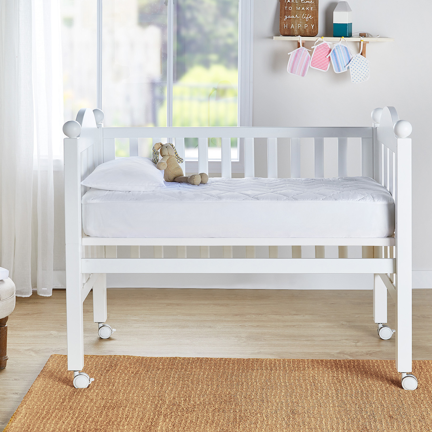 Una cuna blanca con colchón y almohada. Un peluche está sobre el colchón.