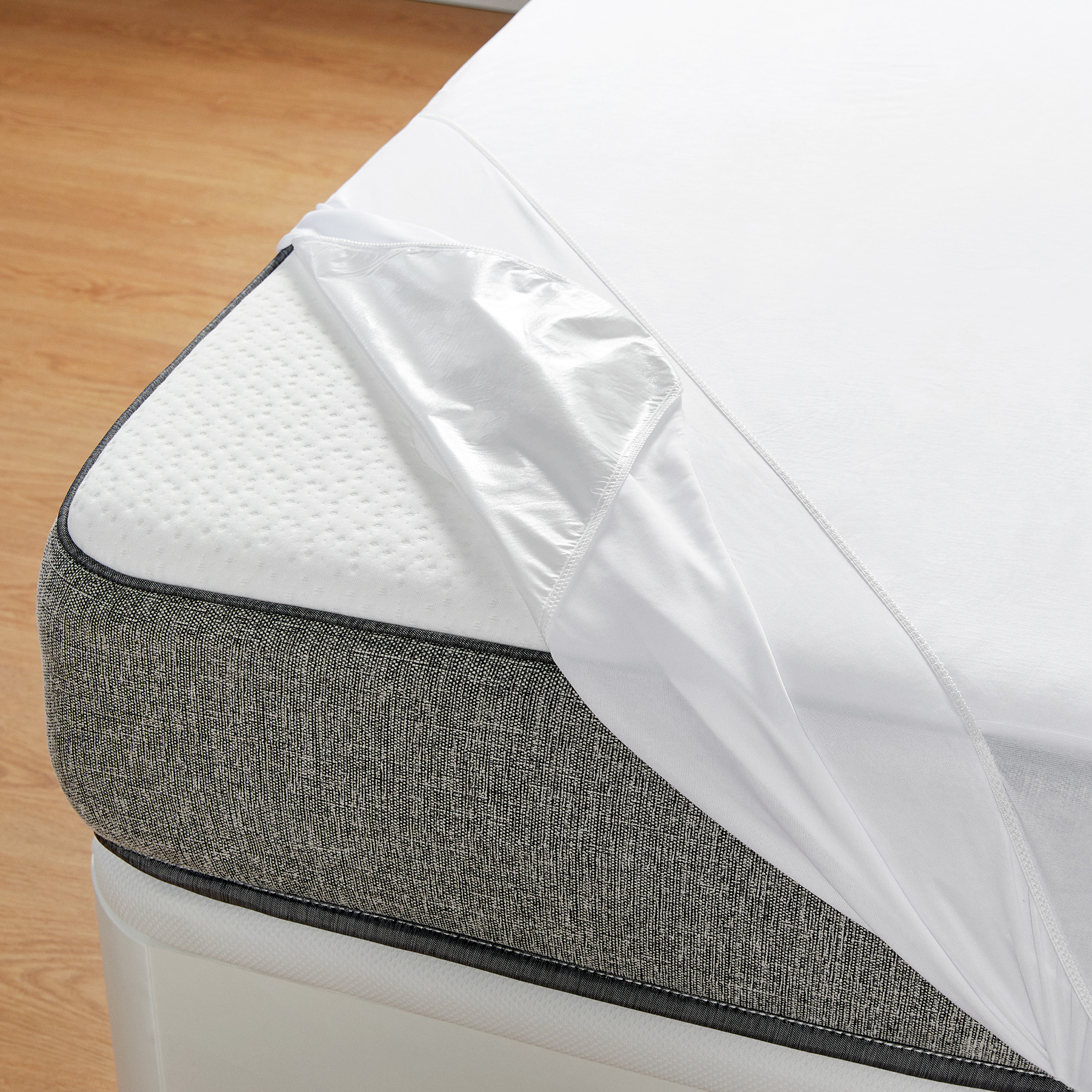 Cama con una sábana blanca parcialmente levantada. El colchón es gris y tiene una superficie texturizada.
