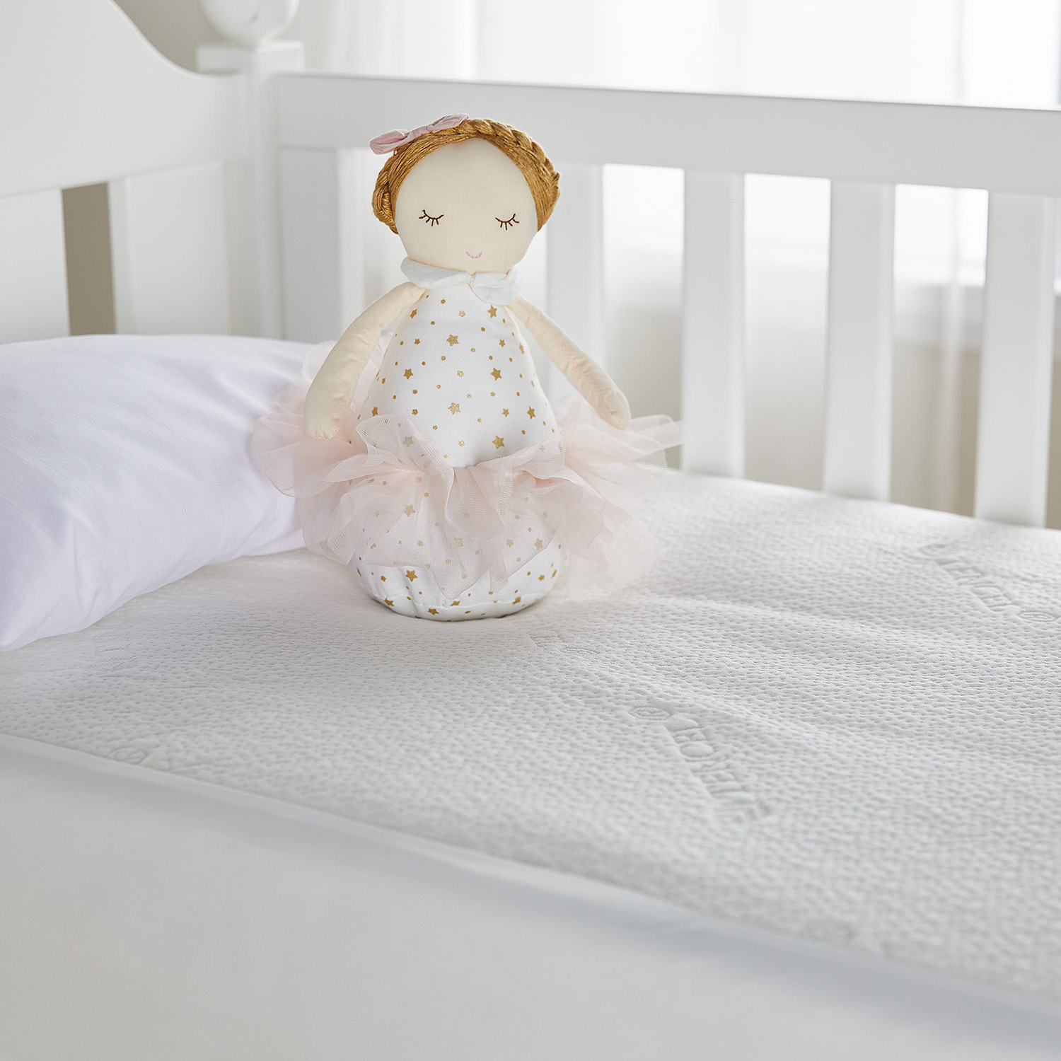 Una muñeca con vestido y lazo en la cabeza descansa sobre un colchón de cuna. El barandal de la cuna es visible.