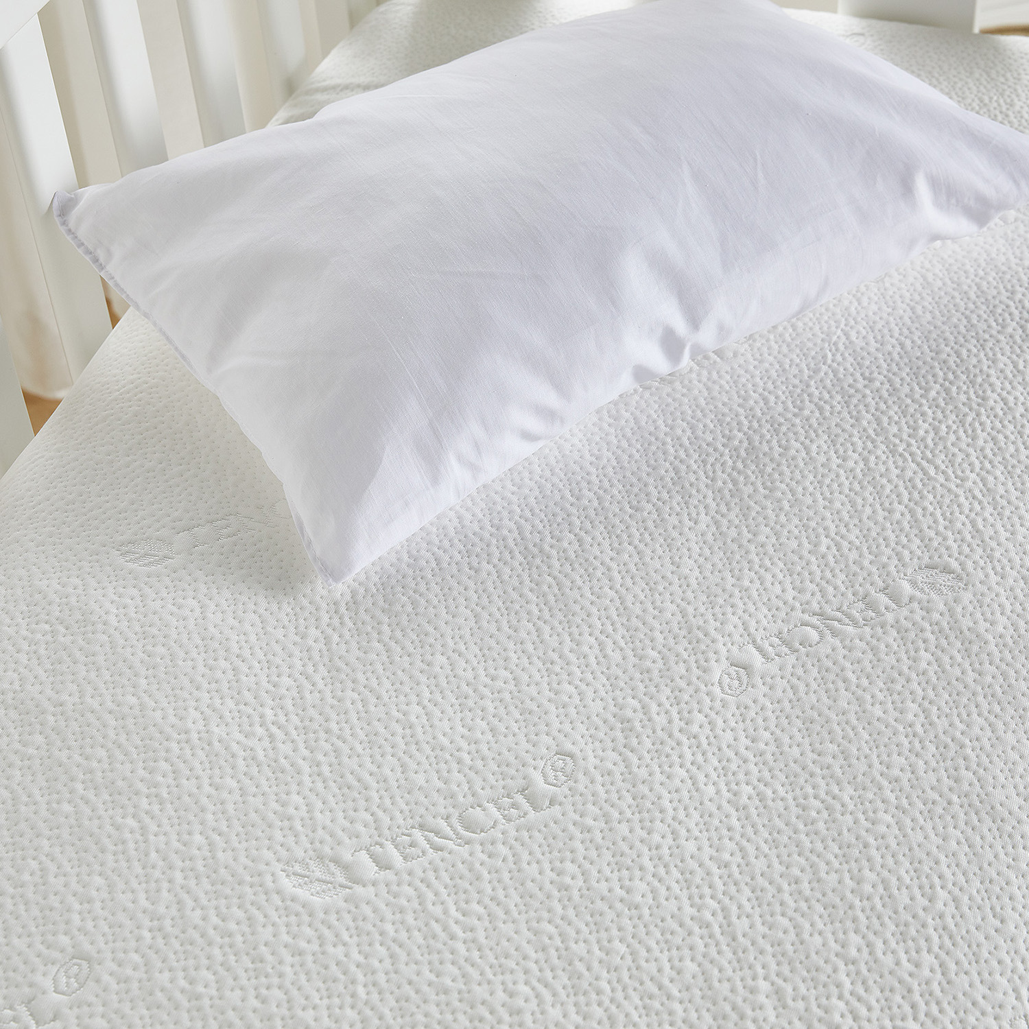 Almohada blanca sobre un colchón blanco texturizado. Un marco de cuna en el fondo.