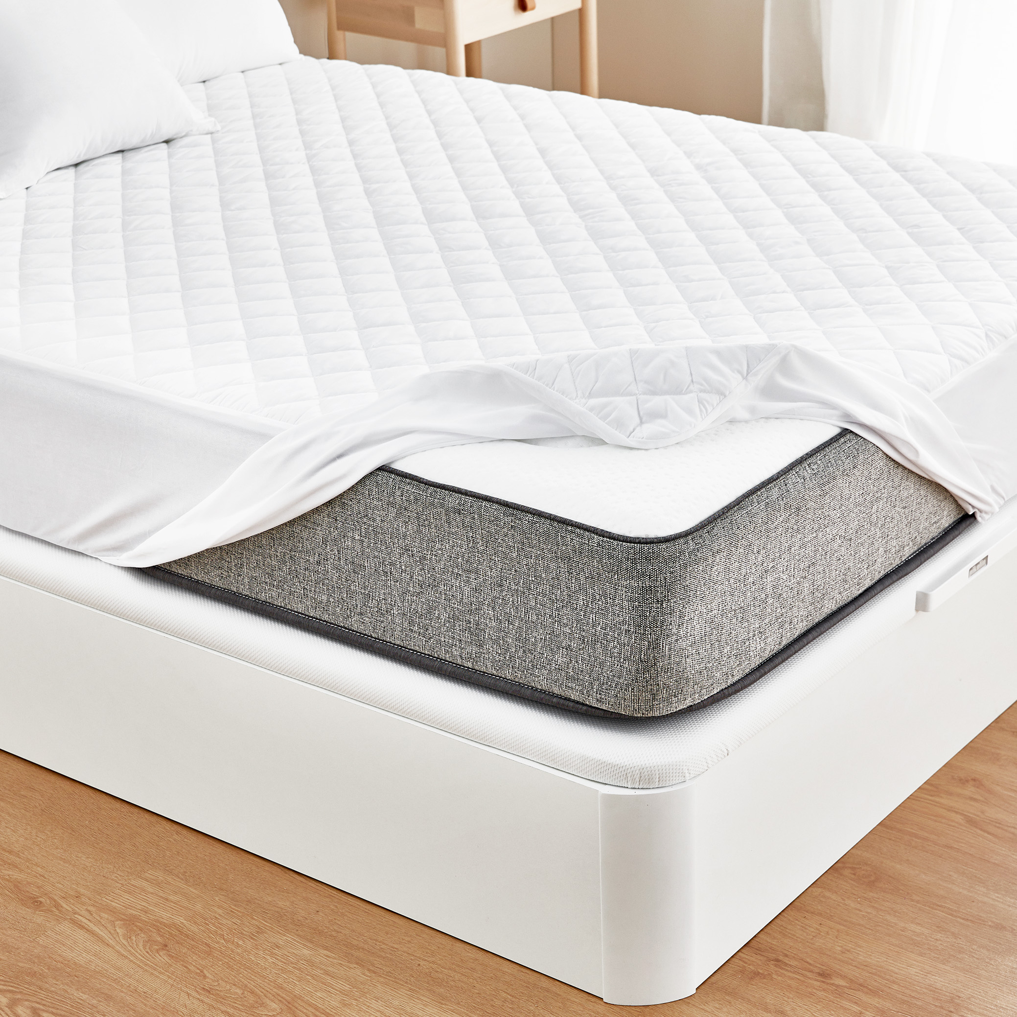Cama con funda de colchón blanca. Edredón blanco parcialmente levantado, mostrando el colchón gris.