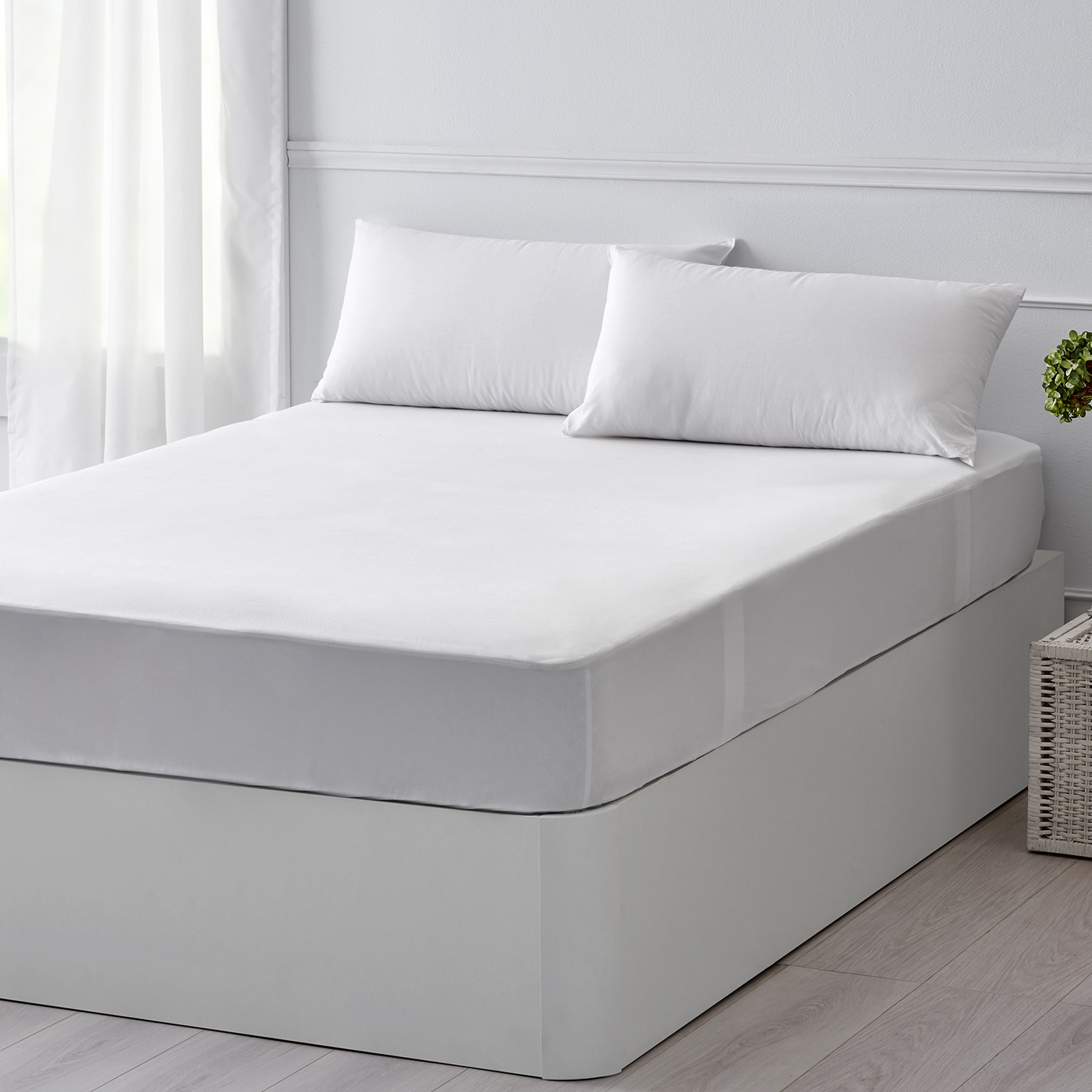Cama blanca con dos almohadas. El fondo incluye una ventana y una planta en maceta.
