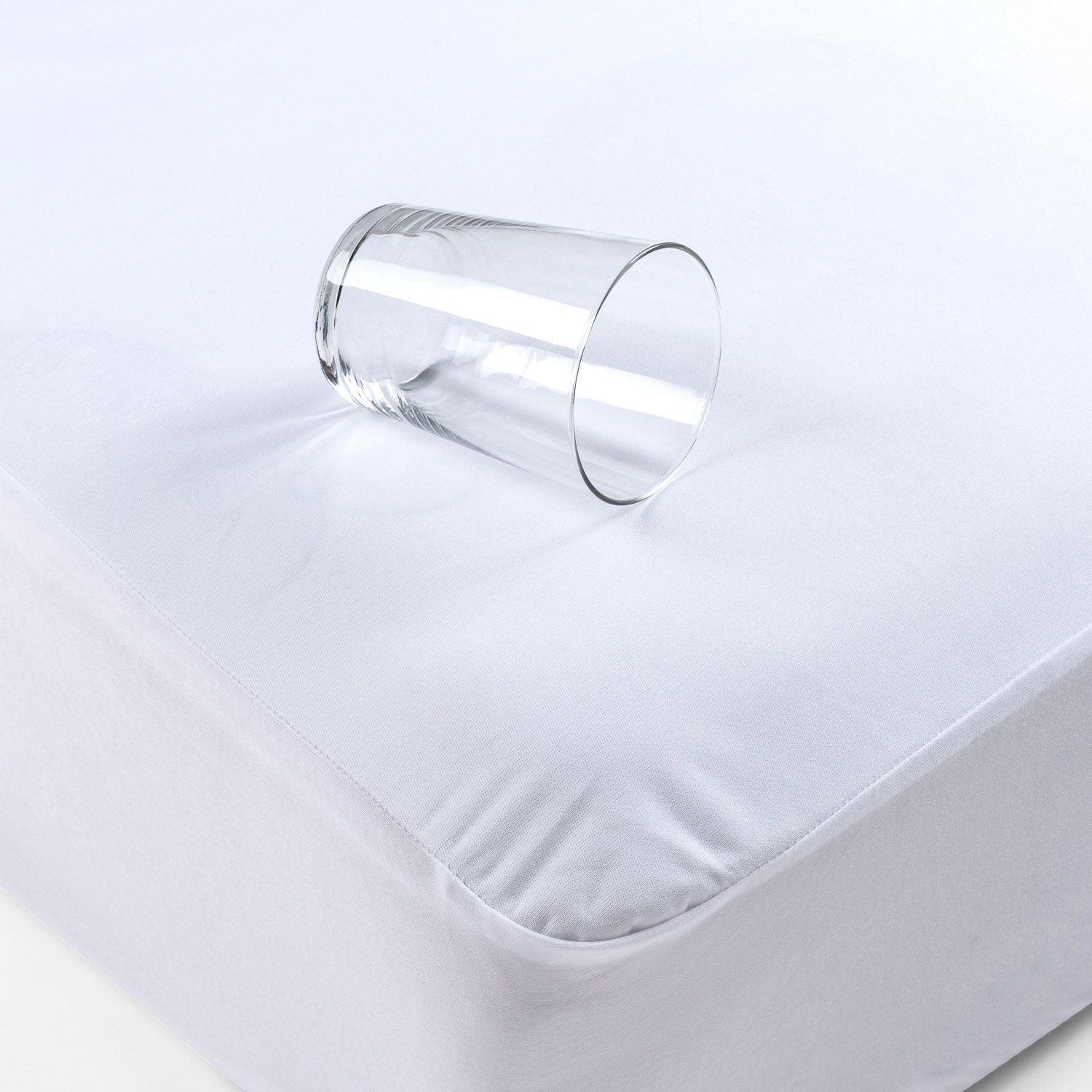 Un vaso transparente inclinado sobre una sábana bajera blanca.