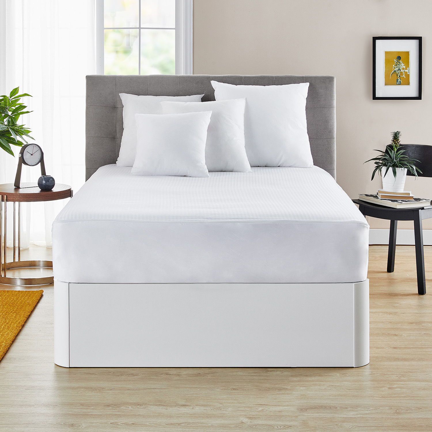 Cama hecha con almohadas blancas, un cubrecama blanco y un cabecero gris. Mesita con decoración.