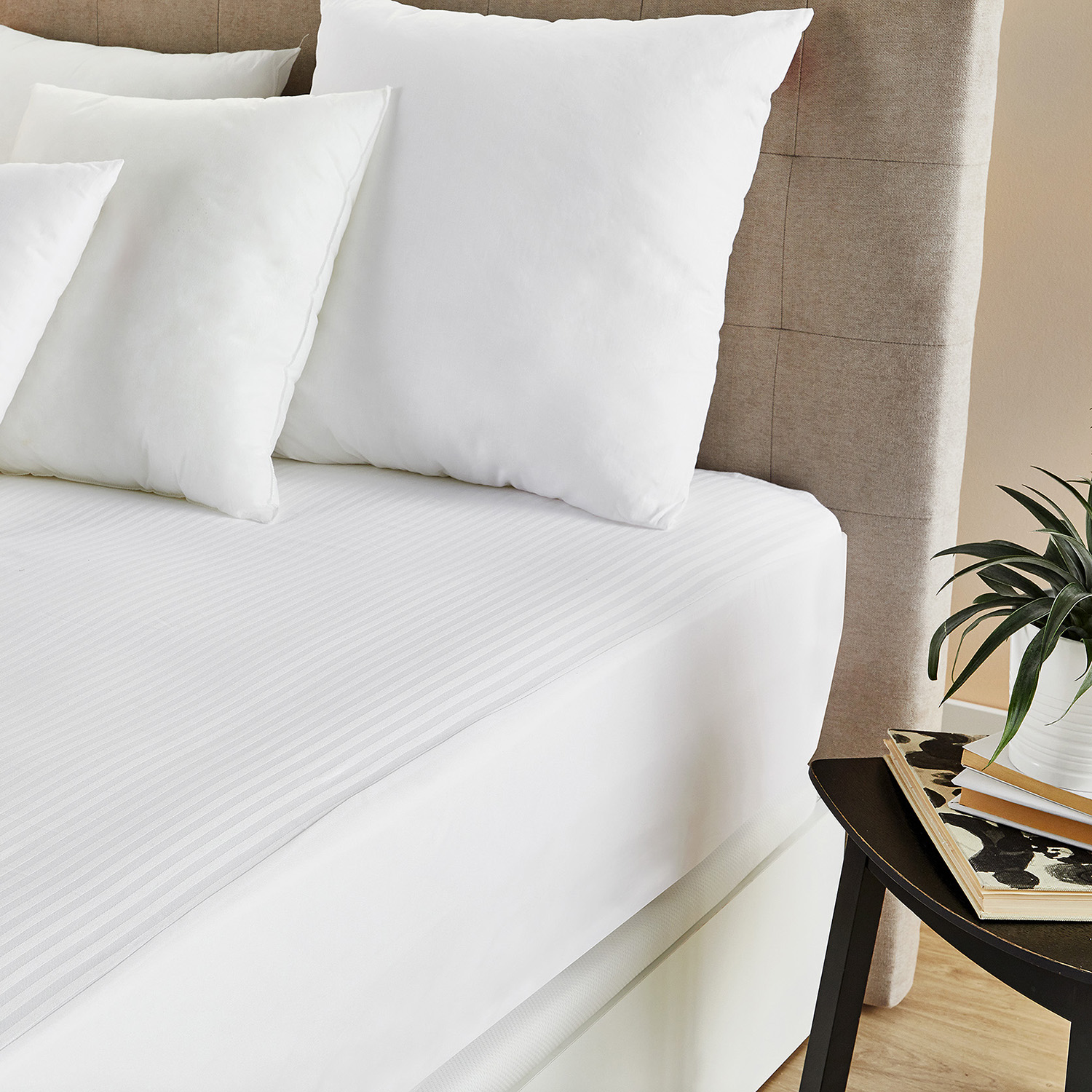 Cama blanca con almohadas. La cama tiene una sábana blanca y un cabecero beige. Hay una mesa al lado.