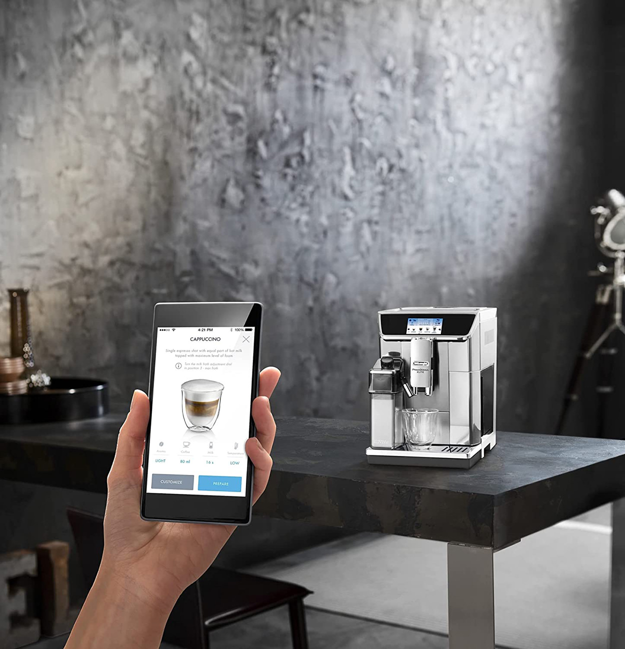 Hand hält Telefon mit Cappuccino-Anleitung neben Kaffeemaschine auf dunklem Tisch.