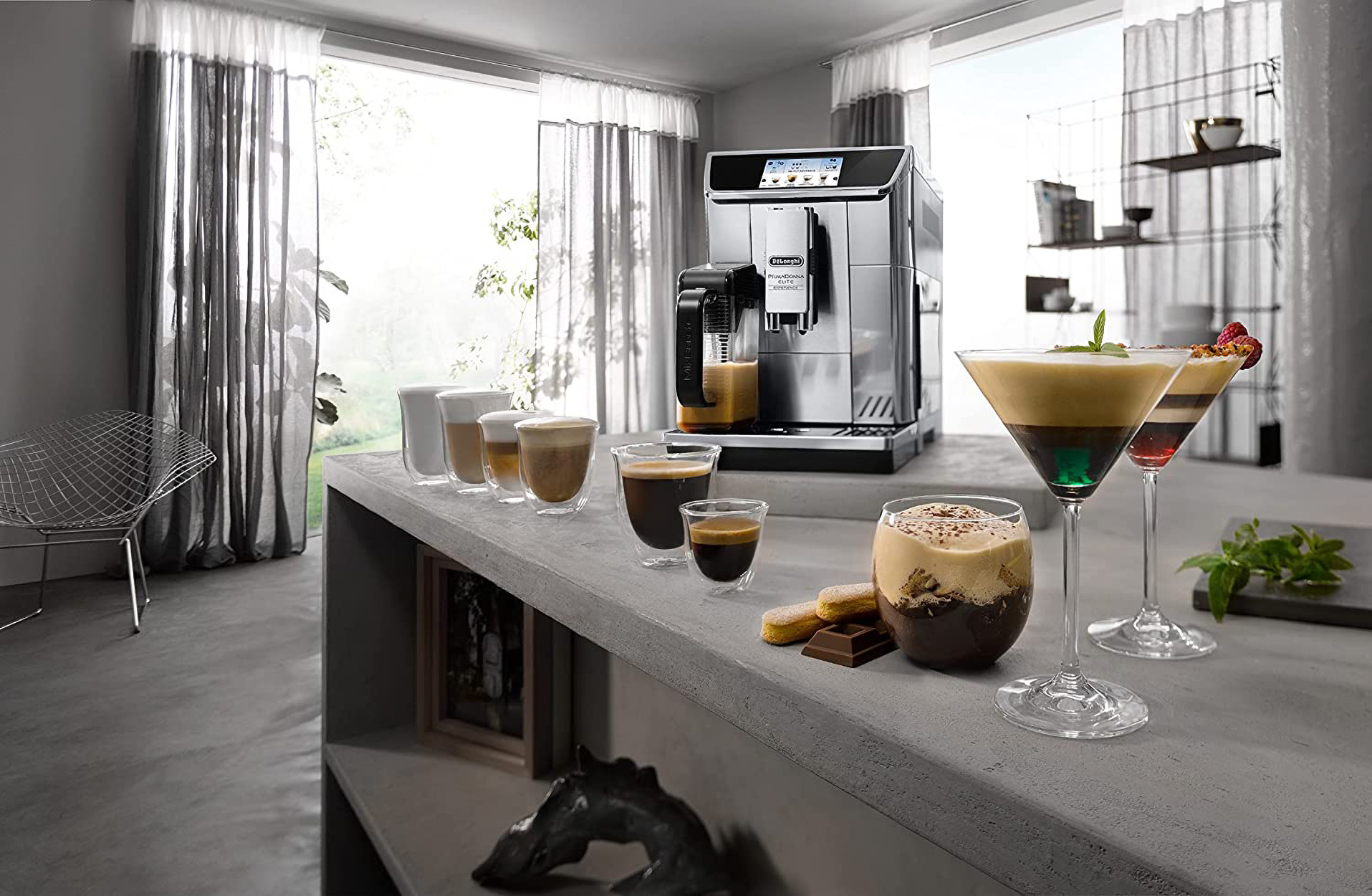 Silberne Espressomaschine brüht Kaffee mit Gläsern Kaffeegetränken davor. Heller Raum mit grauer Theke.
