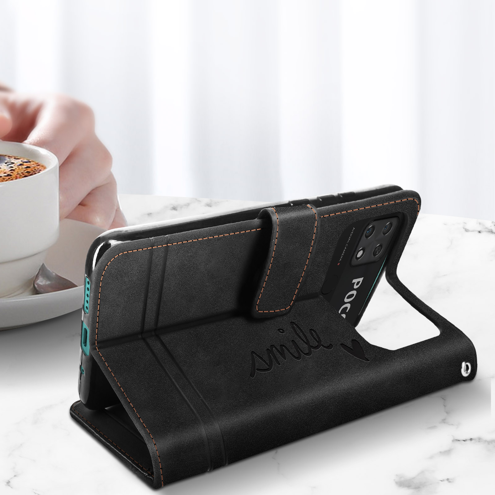 Una custodia per telefono nera è aperta. C'è la parola 'smile' scritta sopra. Una tazza di caffè è accanto.