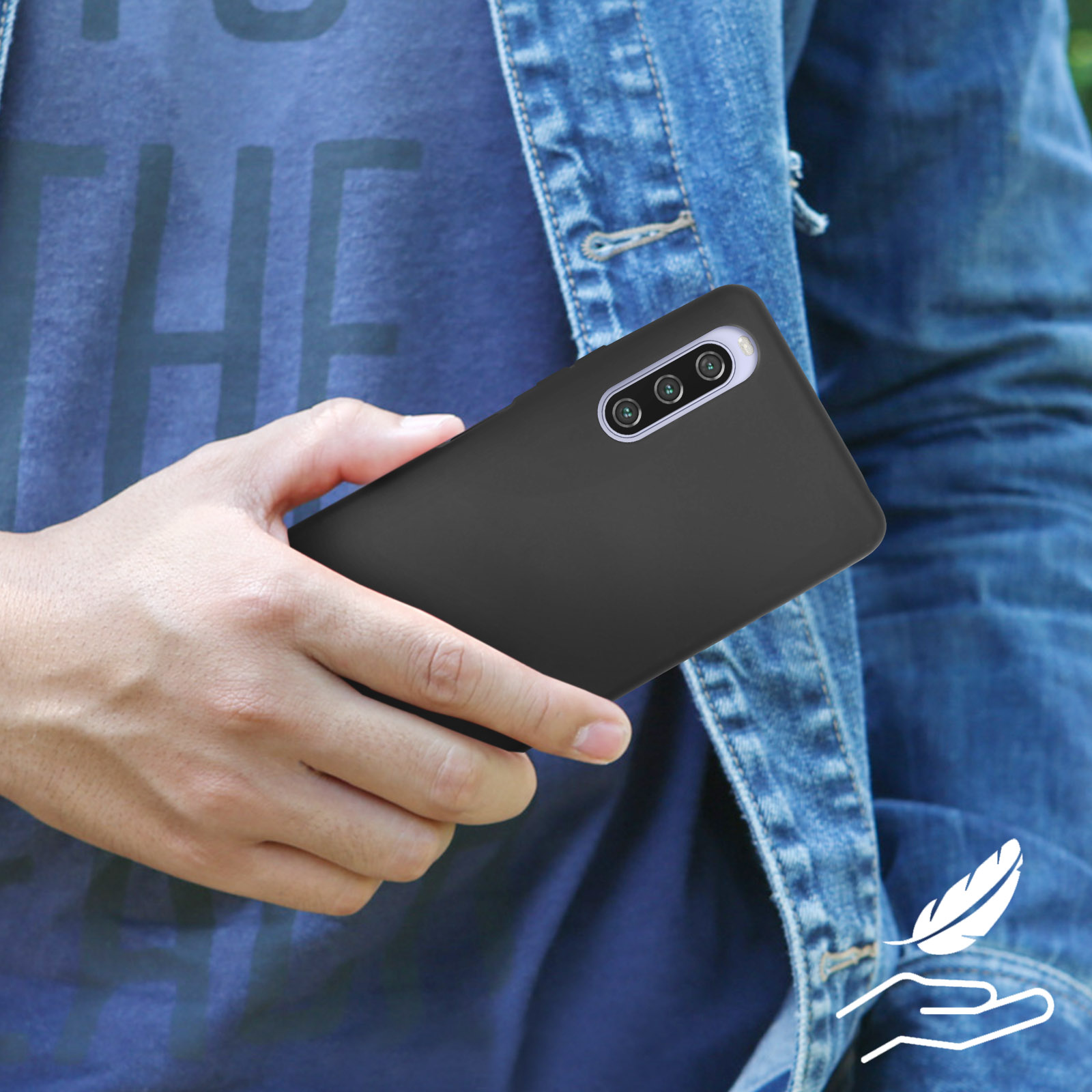 Personne tenant un téléphone noir. La personne porte une veste en jean bleue. Le fond est uni.
