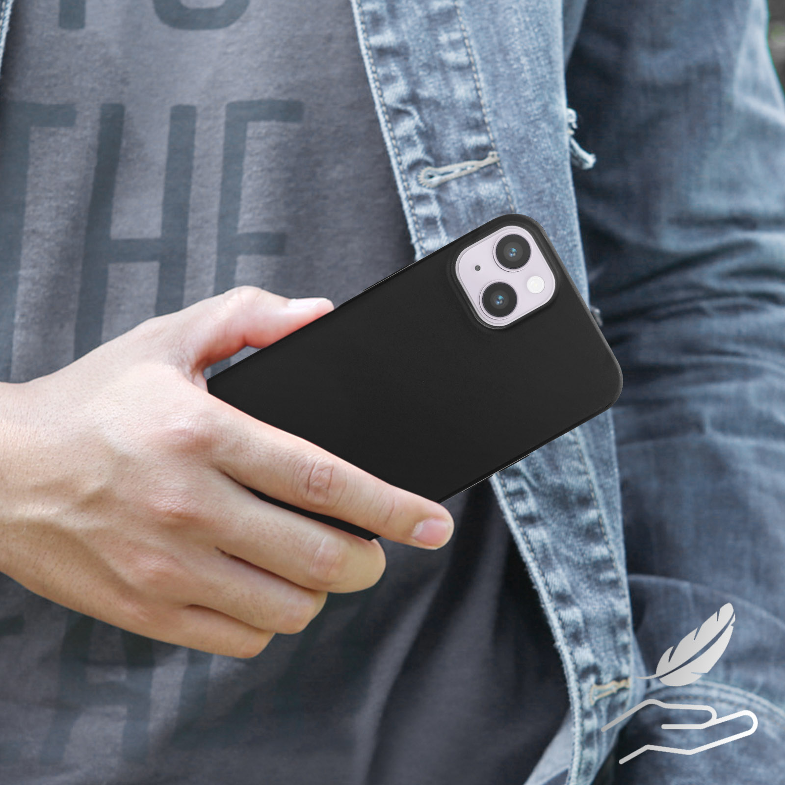 Una persona tiene in mano un telefono nero in una custodia nera. Indossa una giacca di jeans.