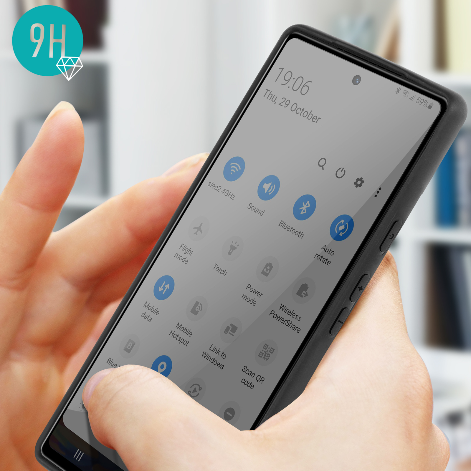 Un téléphone noir affiche son menu de paramètres, tenu en main. L'arrière-plan est flou.