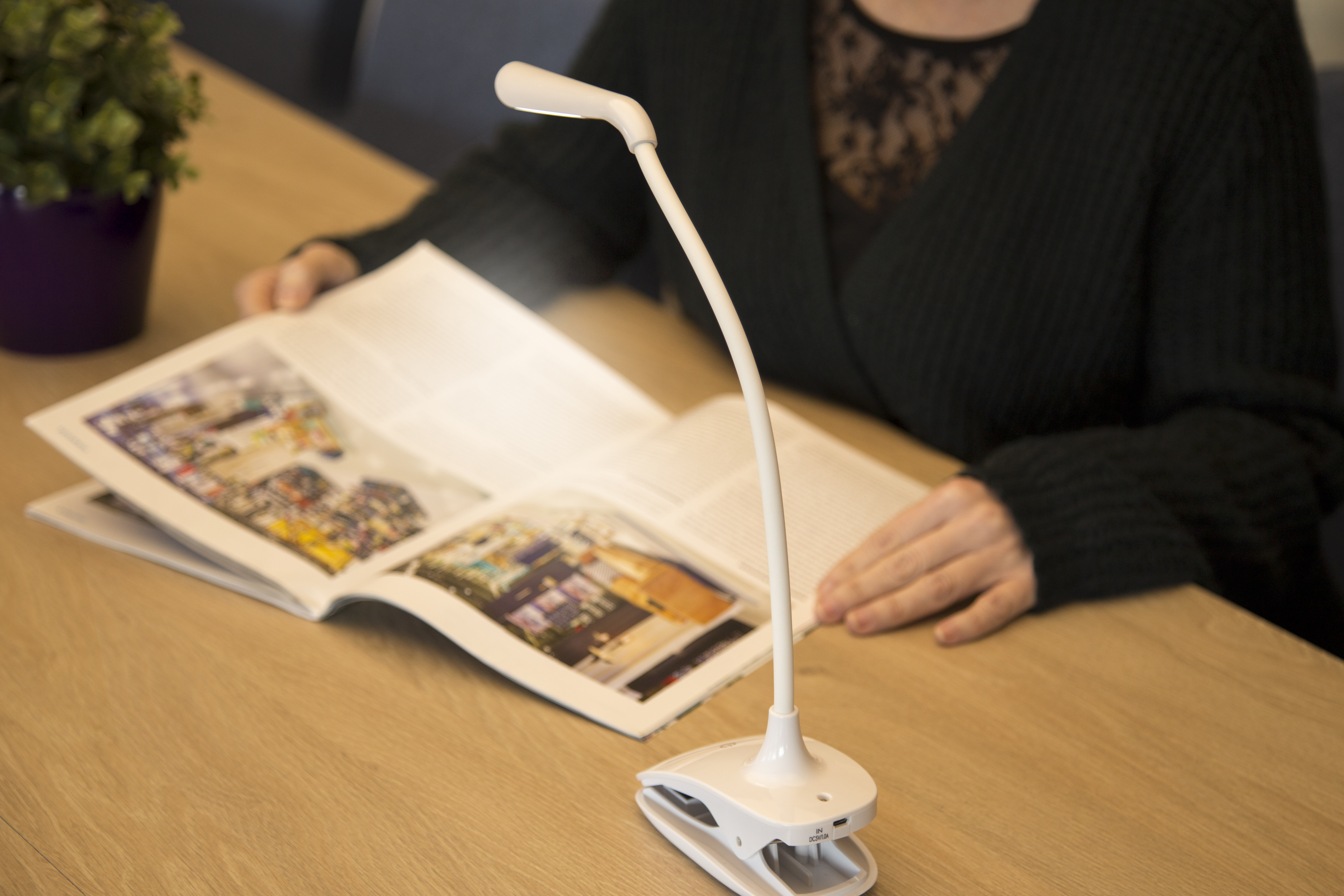 Een bureaulamp is aan een tafel geklikt, die een boek verlicht. Een persoon leest het boek.