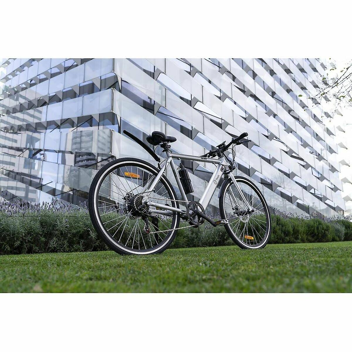 Bicicleta plateada sobre hierba con un edificio moderno al fondo.