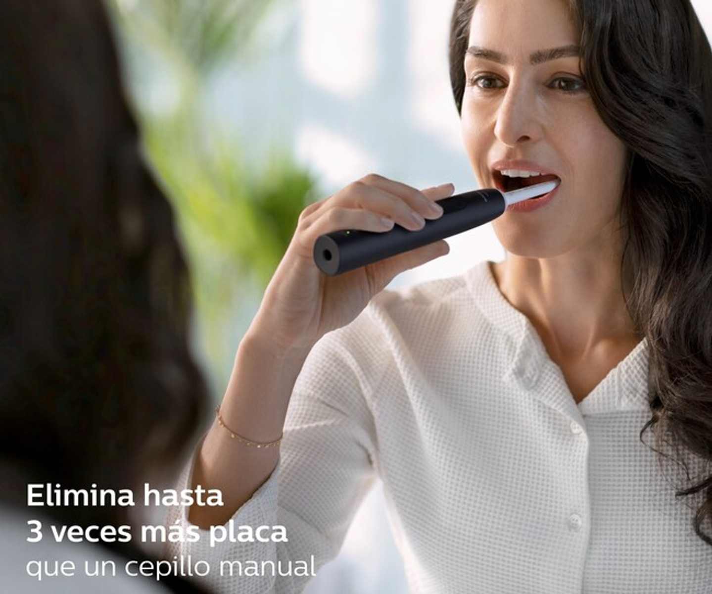 Kobieta myjąca zęby czarną elektryczną szczoteczką. Widoczne odbicie w lustrze. Biała koszula.