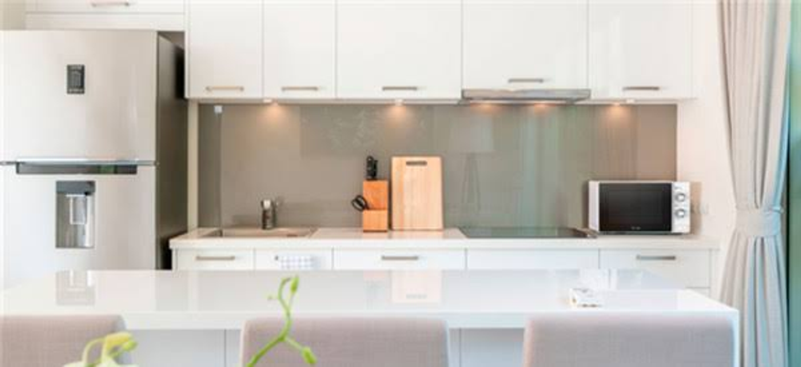 Una cocina con gabinetes blancos, una placa para salpicaduras de acero inoxidable y un microondas. Limpia y moderna.