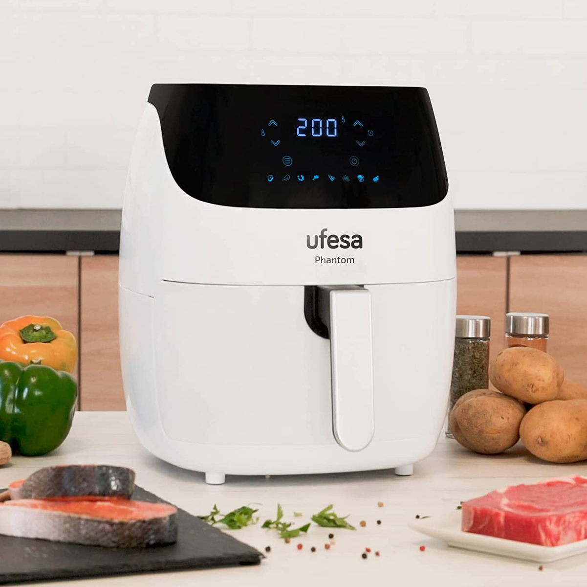 Friggitrice ad aria bianca con cibo su un tavolo. Il display mostra la temperatura. Include salmone, bistecca, verdure e spezie.