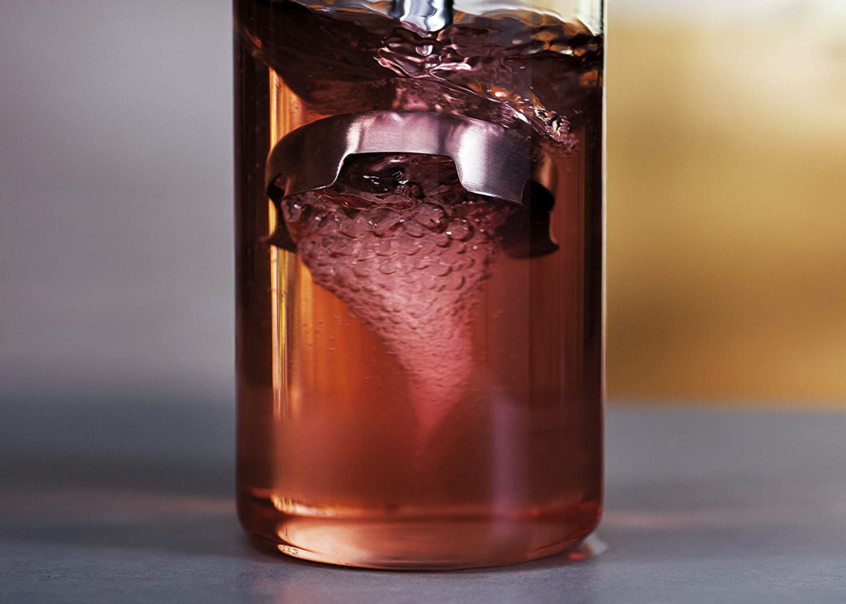Nahaufnahme eines Glases mit rosa Flüssigkeit und einem silbernen Mischgerät, das einen Wirbel erzeugt.