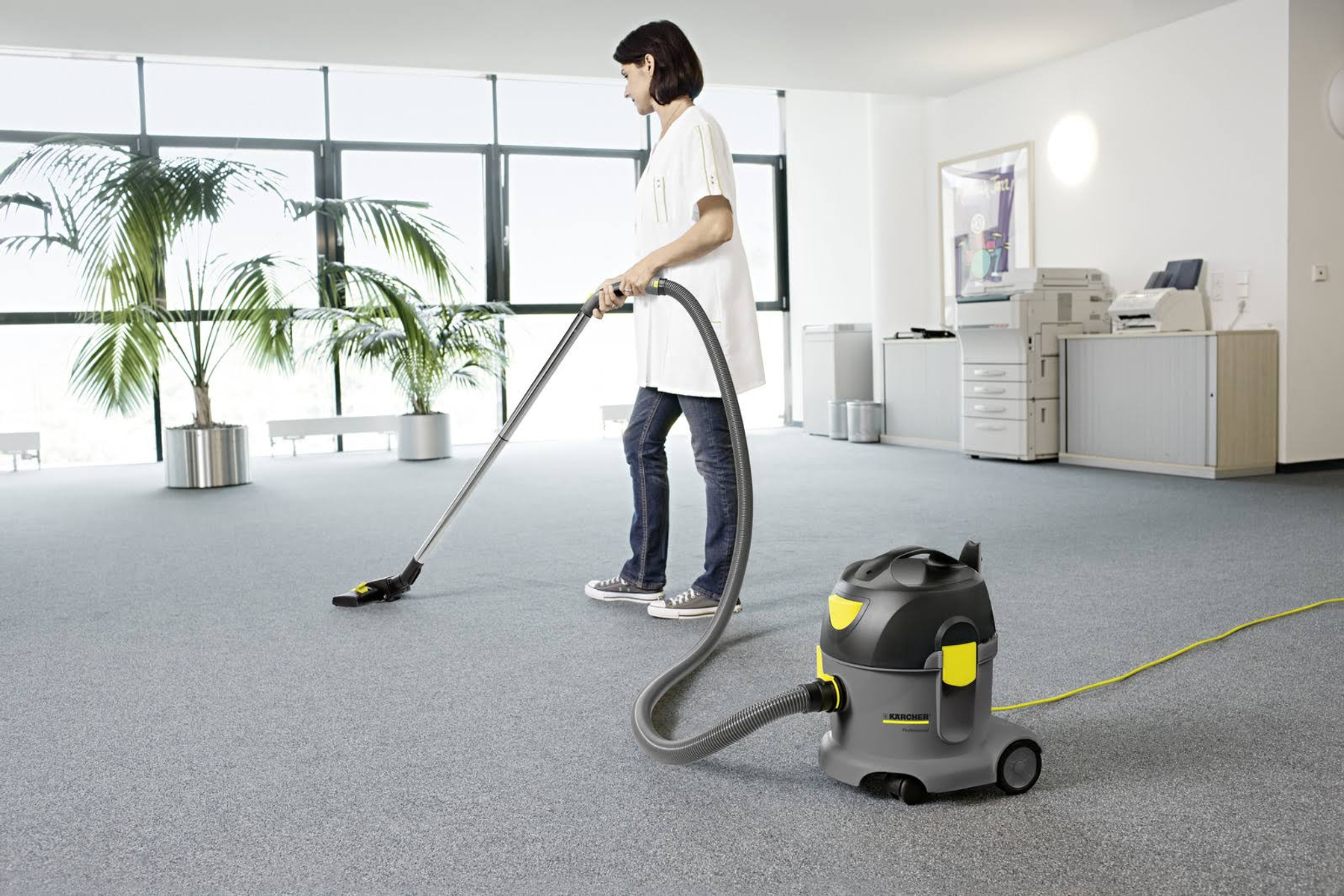 Una donna pulisce un ufficio con un aspirapolvere grigio e giallo.