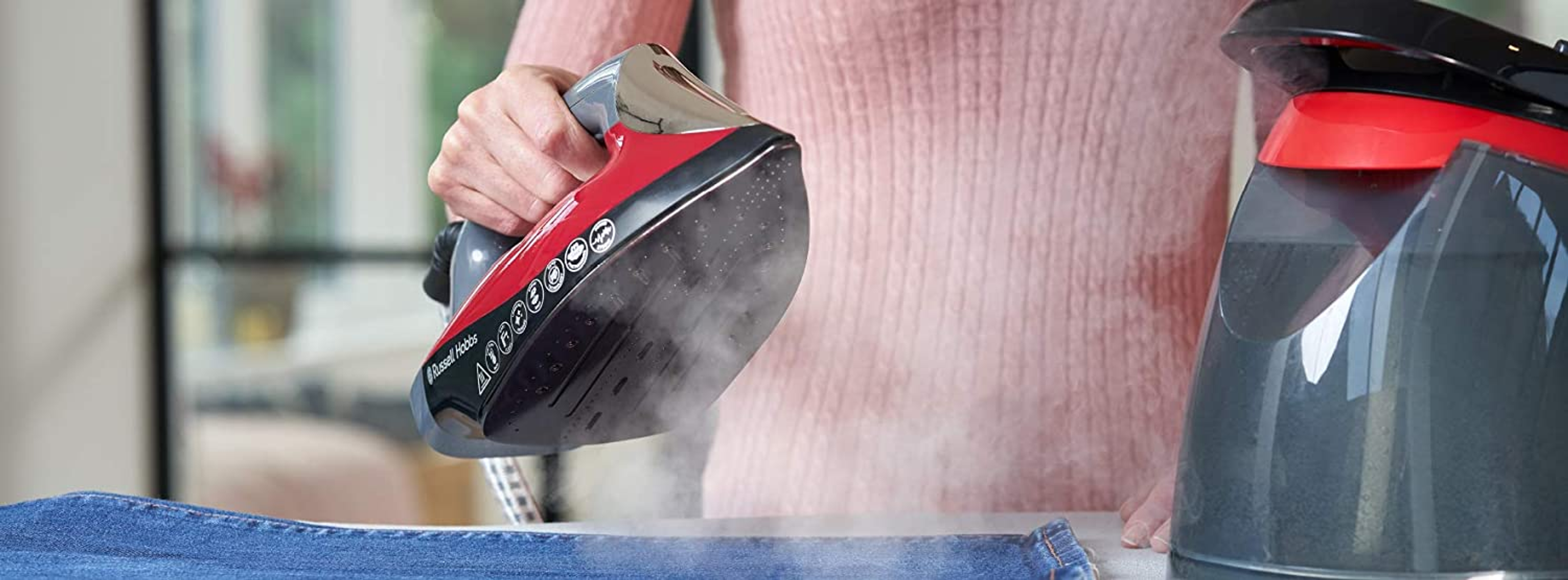 Una mujer planchando mezclilla. La plancha es roja y negra, y el vapor es visible.