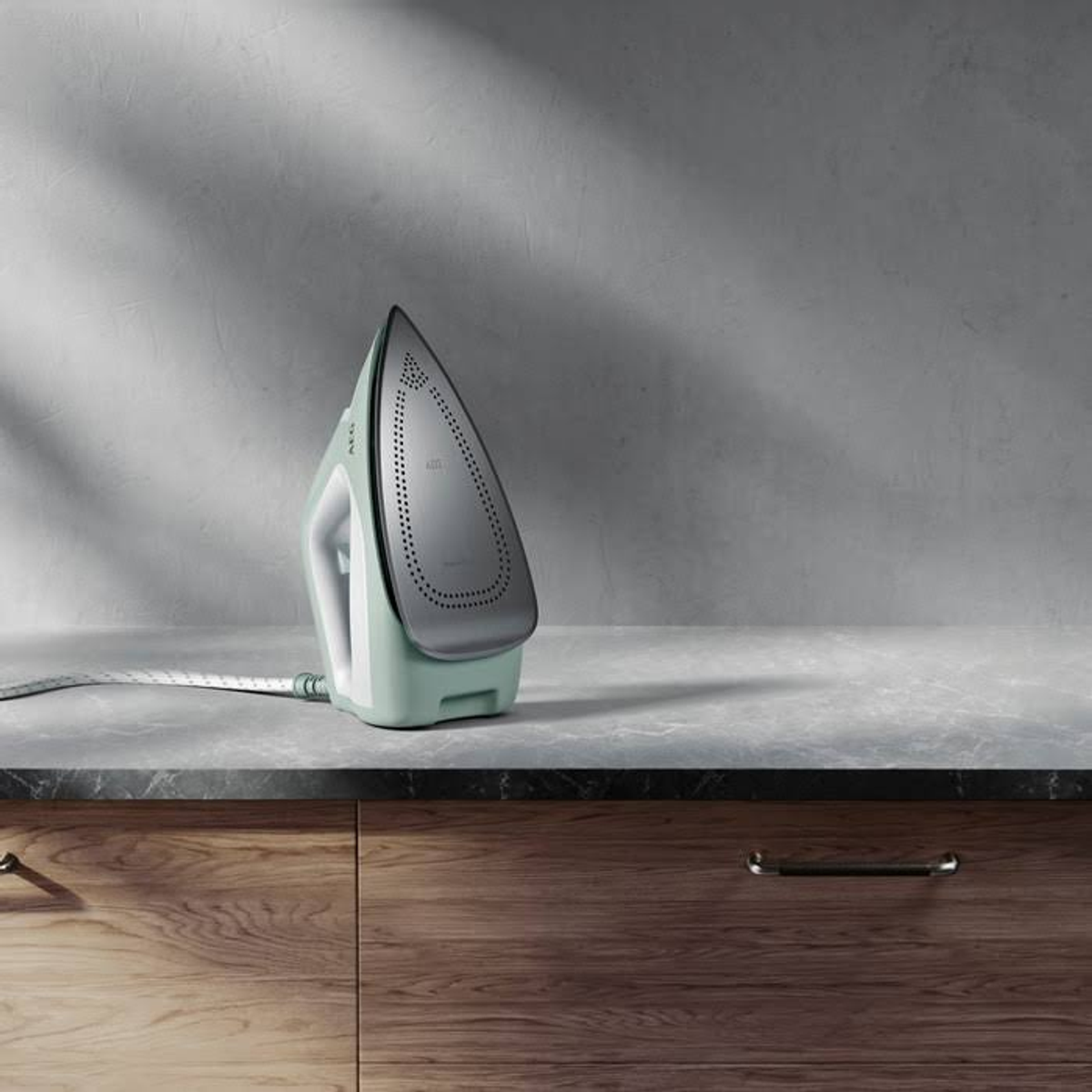 Bügeleisen auf einer Theke. Der Hintergrund ist eine hellgraue Wand und ein Holzschrank.