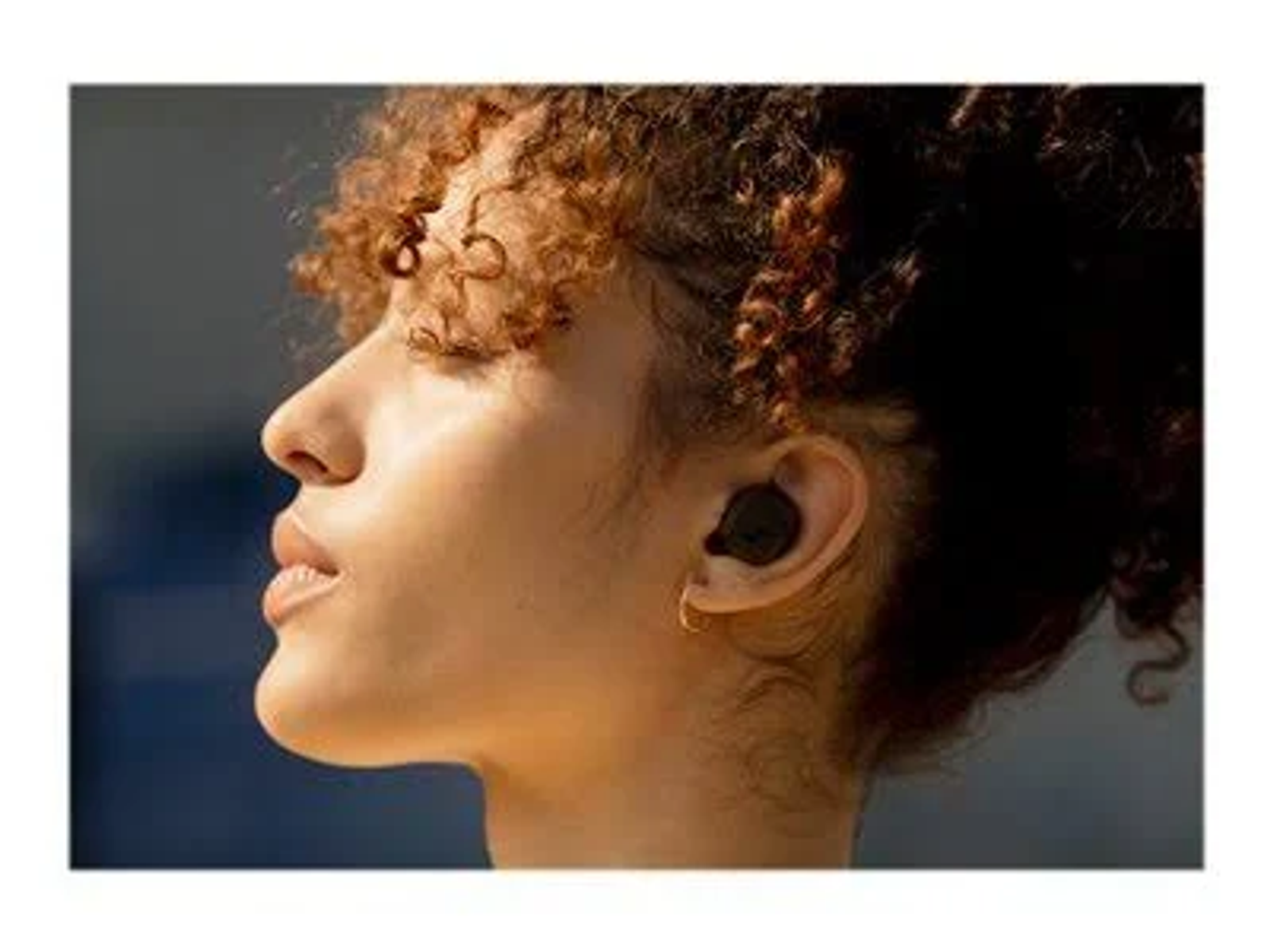 Una foto de perfil de una mujer que lleva auriculares negros en la oreja, con un fondo borroso.
