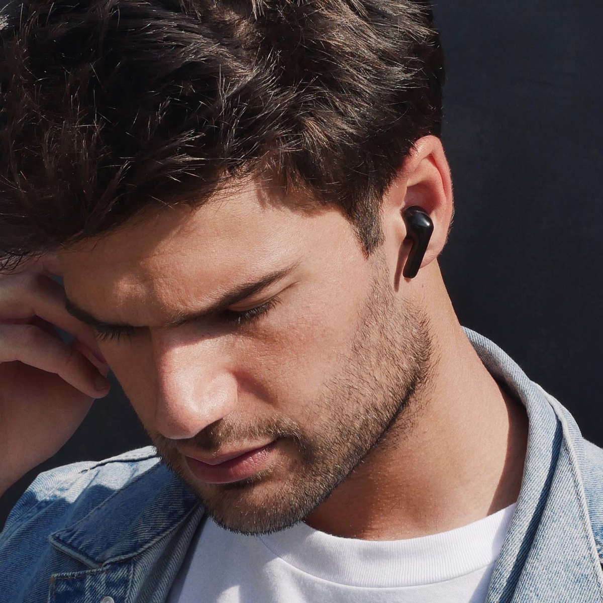 Mężczyzna w dżinsowej kurtce, z czarną słuchawką w prawym uchu.