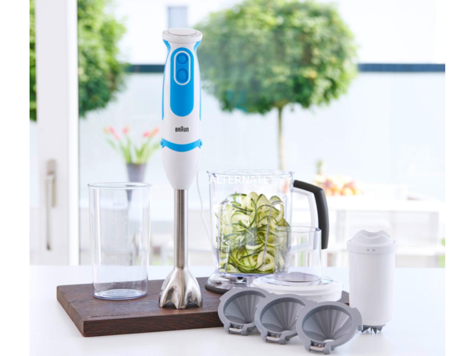 Un frullatore a immersione con accessori. C'è un contenitore trasparente con zucchine a fette.