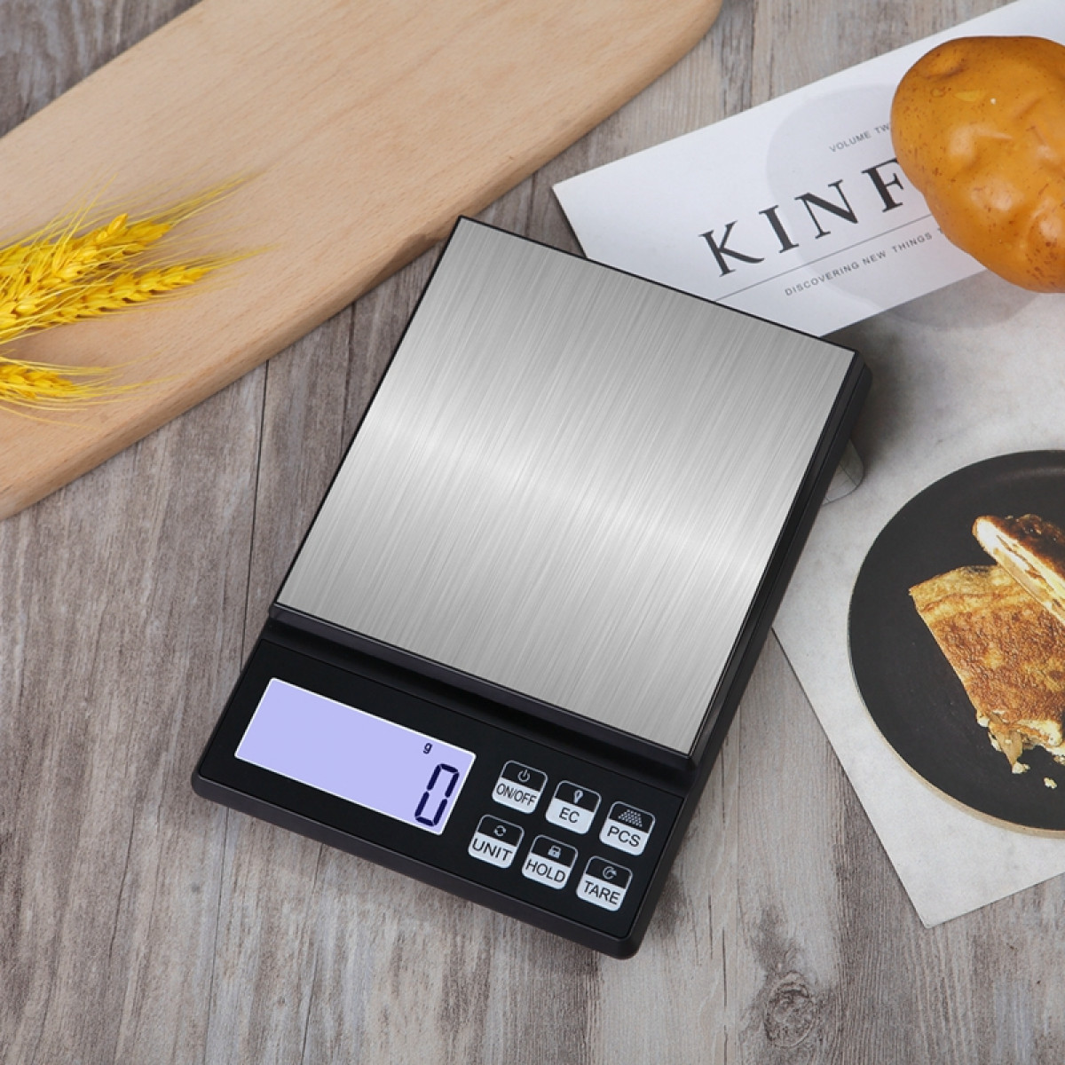 Cyfrowa waga kuchenna z metalowym blatem, czarną podstawą i wyświetlaczem LCD. Jedzenie w tle.