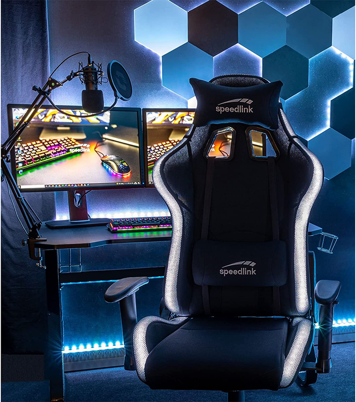 Configuración gaming con silla, monitores, micrófono y fondo colorido.