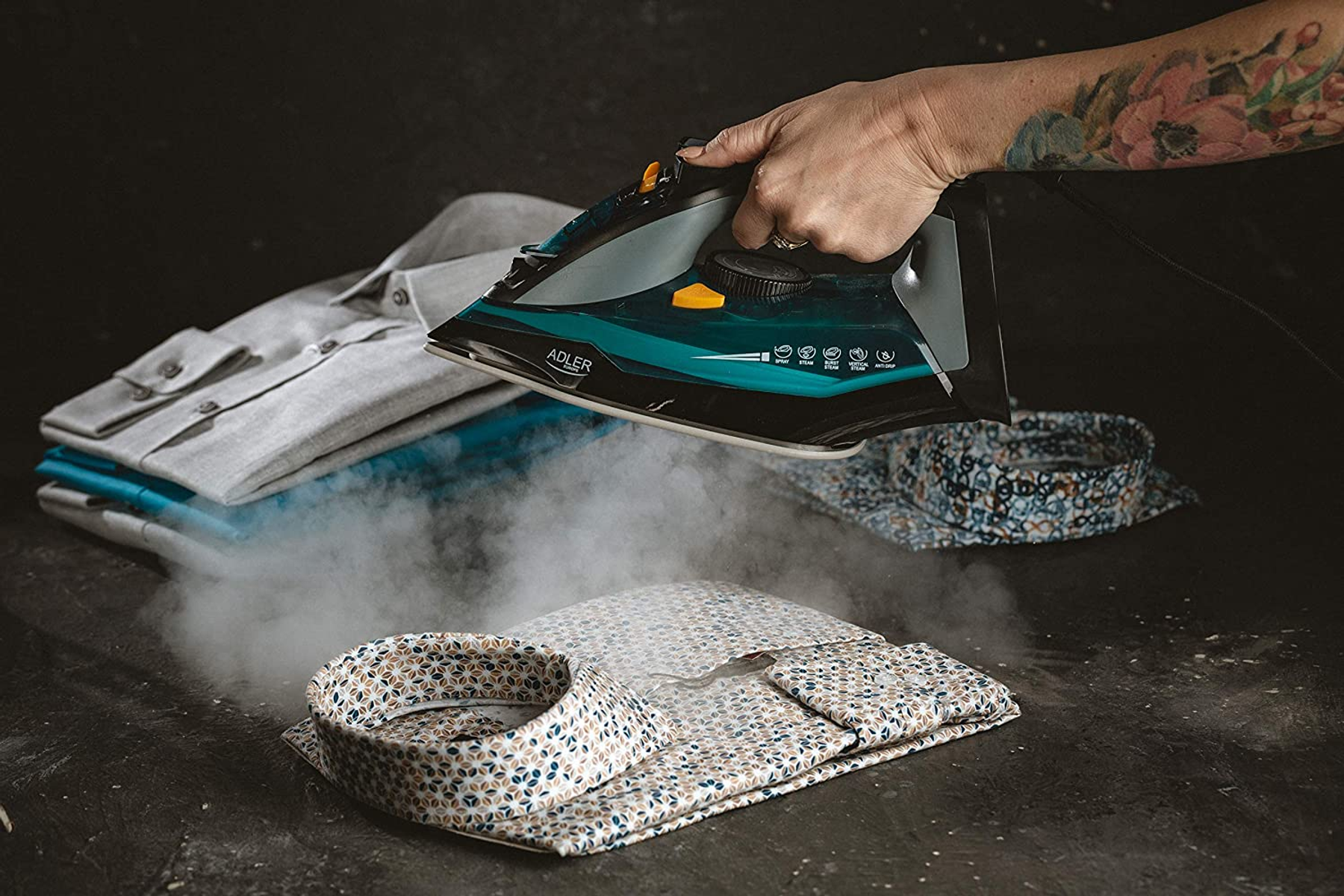 Osoba prasuje koszule parą. Na ciemnej powierzchni są złożone i rozłożone koszule.