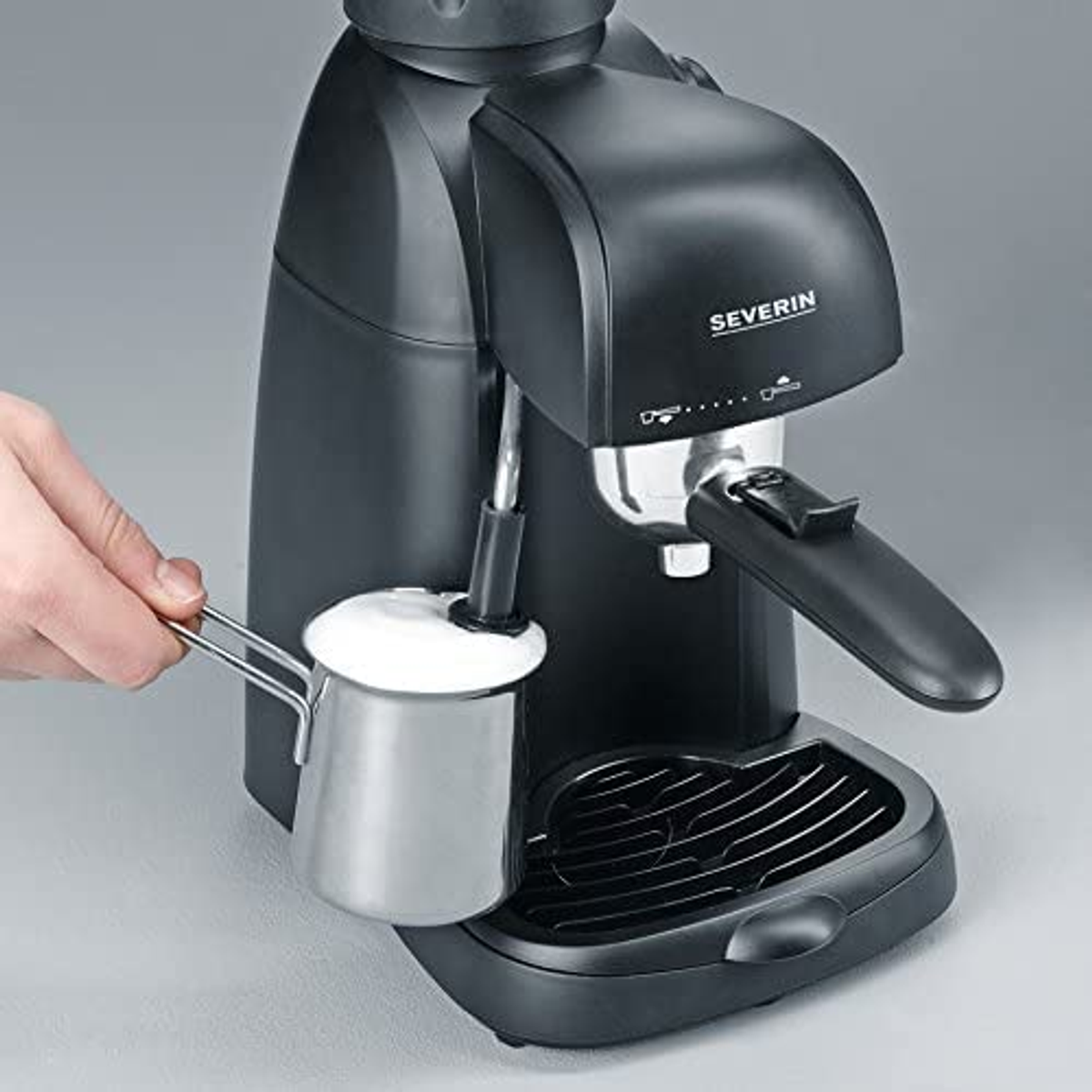 Espressomaschine mit einer Hand, die einen Milchaufschäumer hält, schwarzer Hintergrund.